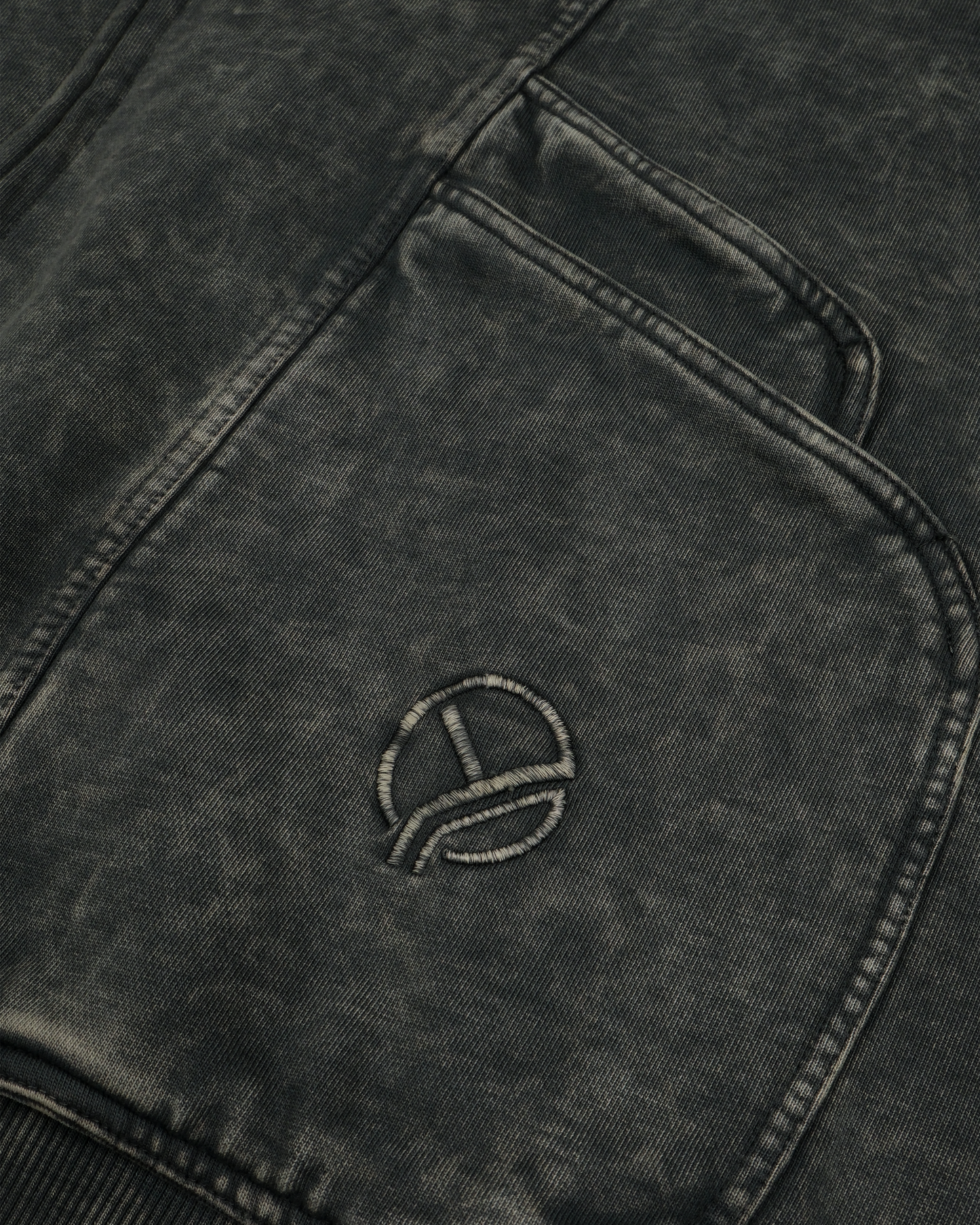 Nahaufnahme einer diagonalen Naht und der Taschenkante eines grauen Zip-Hoodies mit Washed-Effekt. Die Textur des Stoffes ist deutlich sichtbar, die Nahtlinien und der ausgewaschene Farbverlauf erzeugen eine