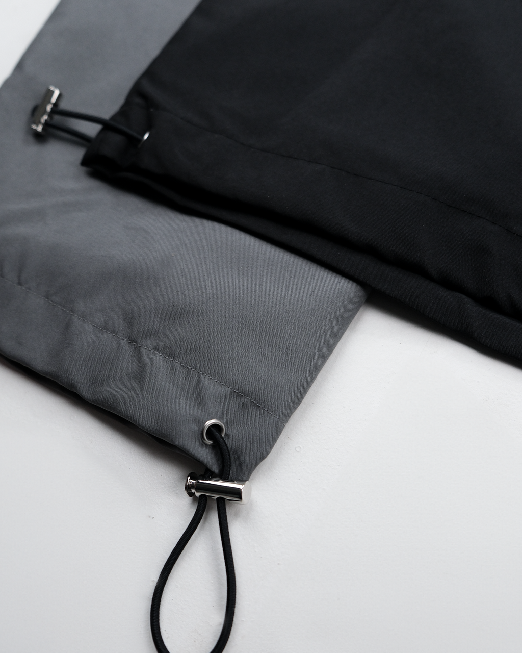 Nahaufnahme des Saums mit integriertem Kordelzug zur Weitenregulierung. Zu sehen ist ein silberner Stopper mit Öse und eingezogenem, schwarzem Band.

