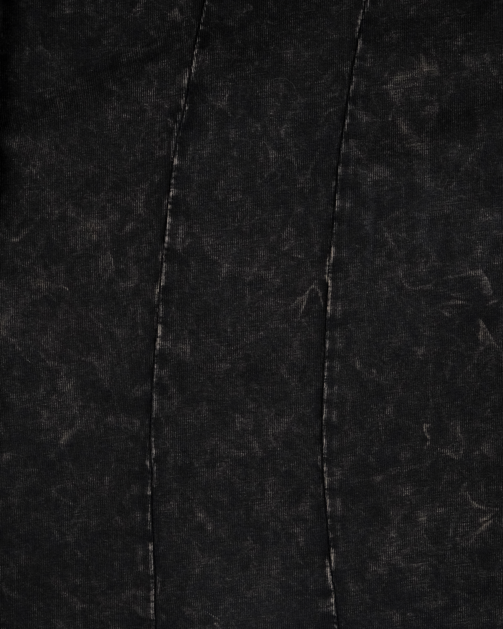  Detailansicht des Shirts. Der Stoff ist in verwaschenem Schwarz gehalten, die umliegende Naht ist sichtbar verarbeitet.