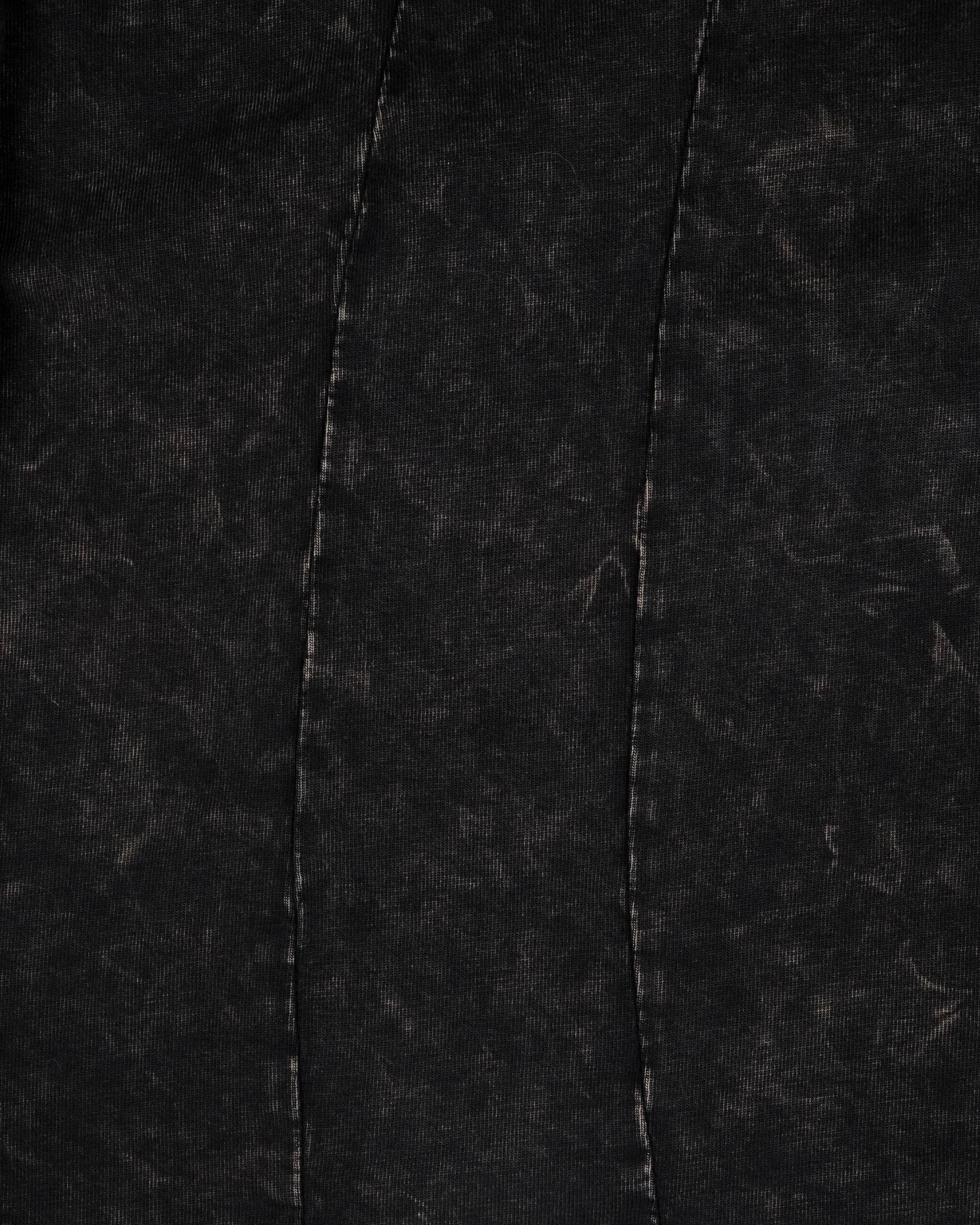  Detailansicht des Shirts. Der Stoff ist in verwaschenem Schwarz gehalten, die umliegende Naht ist sichtbar verarbeitet.