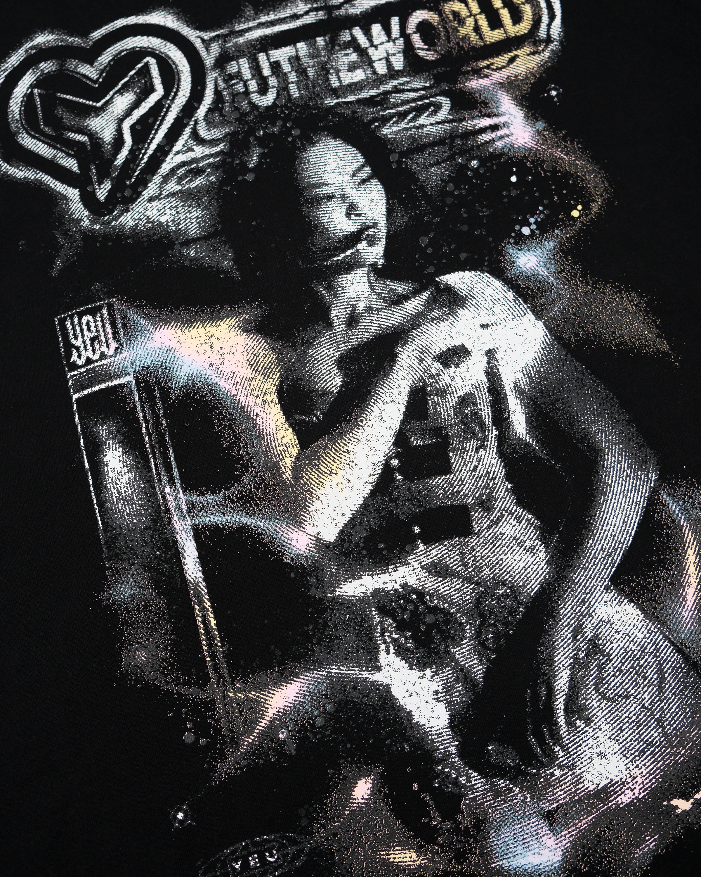 Nahaufnahme des T-Shirt-Prints mit detailreicher Textur. Die schwarz-weiße Frauenfigur ist von körnigen Glanzeffekten, violetten und goldenen Lichtverläufen sowie typografischen Elementen umgeben. Oben ist das „YEU THE WORLD“-Logo eingebettet, darunter der Schriftzug „YEU“ auf einem seitlich stehenden Balken. Die Druckqualität ist strukturiert und leicht glänzend.
