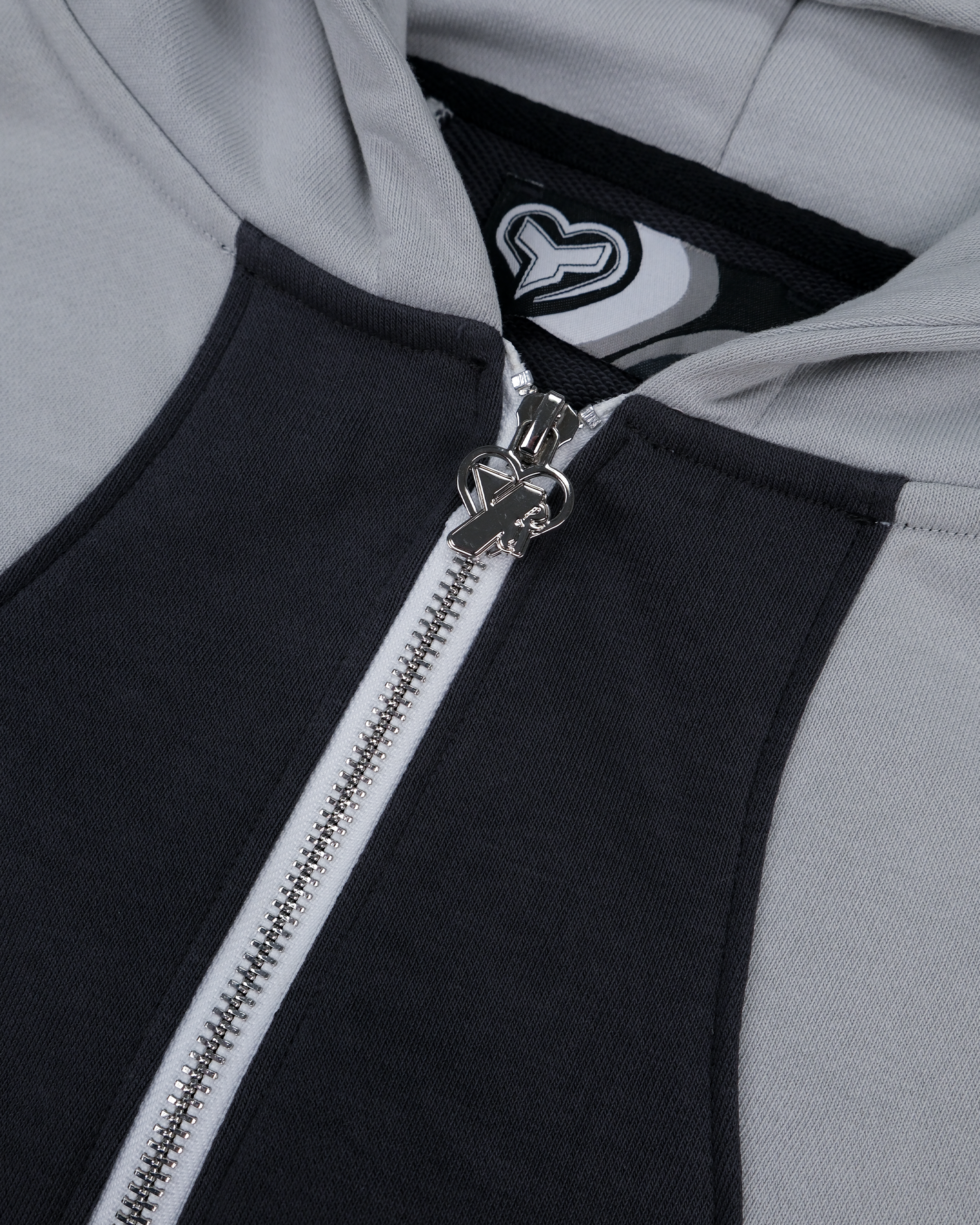 Detailaufnahme des silberfarbenen Reißverschlusses mit herzförmigem Logo-Zipper, umgeben von schwarz-weißen Einsatzflächen. Im Inneren sichtbar ist das Etikett mit stilisiertem Herzsymbol auf gestreiftem Label.