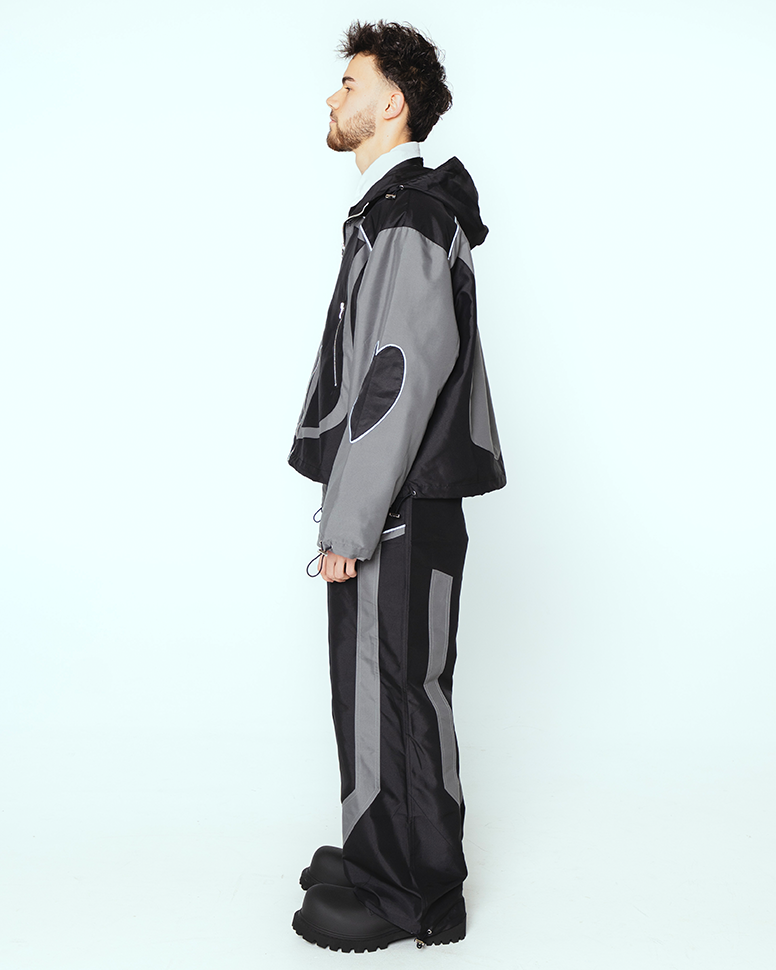 Rechte Seitenansicht der Jacke, identisch wie links: der rechte Ärmel trägt ebenfalls ein appliziertes Herzmotiv. Die Ziernähte und Einsätze folgen der Körperlinie, während die Hose durch seitliche Farbflächen betont wird.

