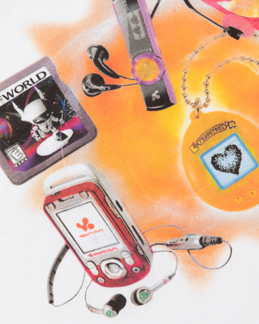 Nahaufnahme des Frontprints auf dem weißen T-Shirt. Der Druck zeigt mehrere farbige Retro-Objekte, darunter ein rotes Klapphandy, Ohrhörer, ein lilafarbener MP3-Player, ein gelbes Tamagotchi und eine Spielkassette.