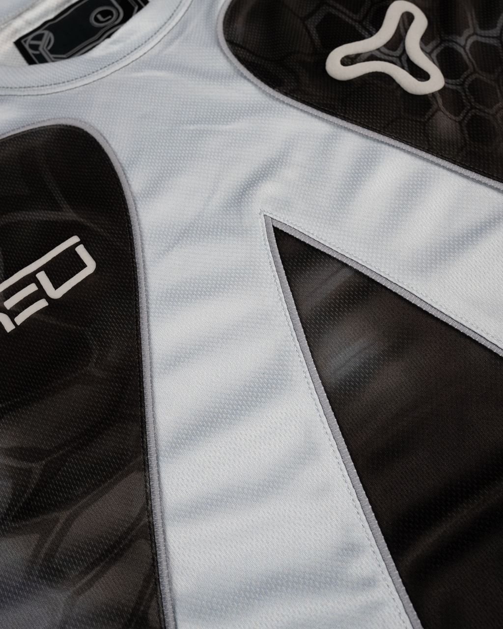 Nahaufnahme der strukturierten Materialoberfläche mit geschwungenen Nahtlinien und platziertem YEU-Logo sowie Markenemblem auf schwarzem Grund.