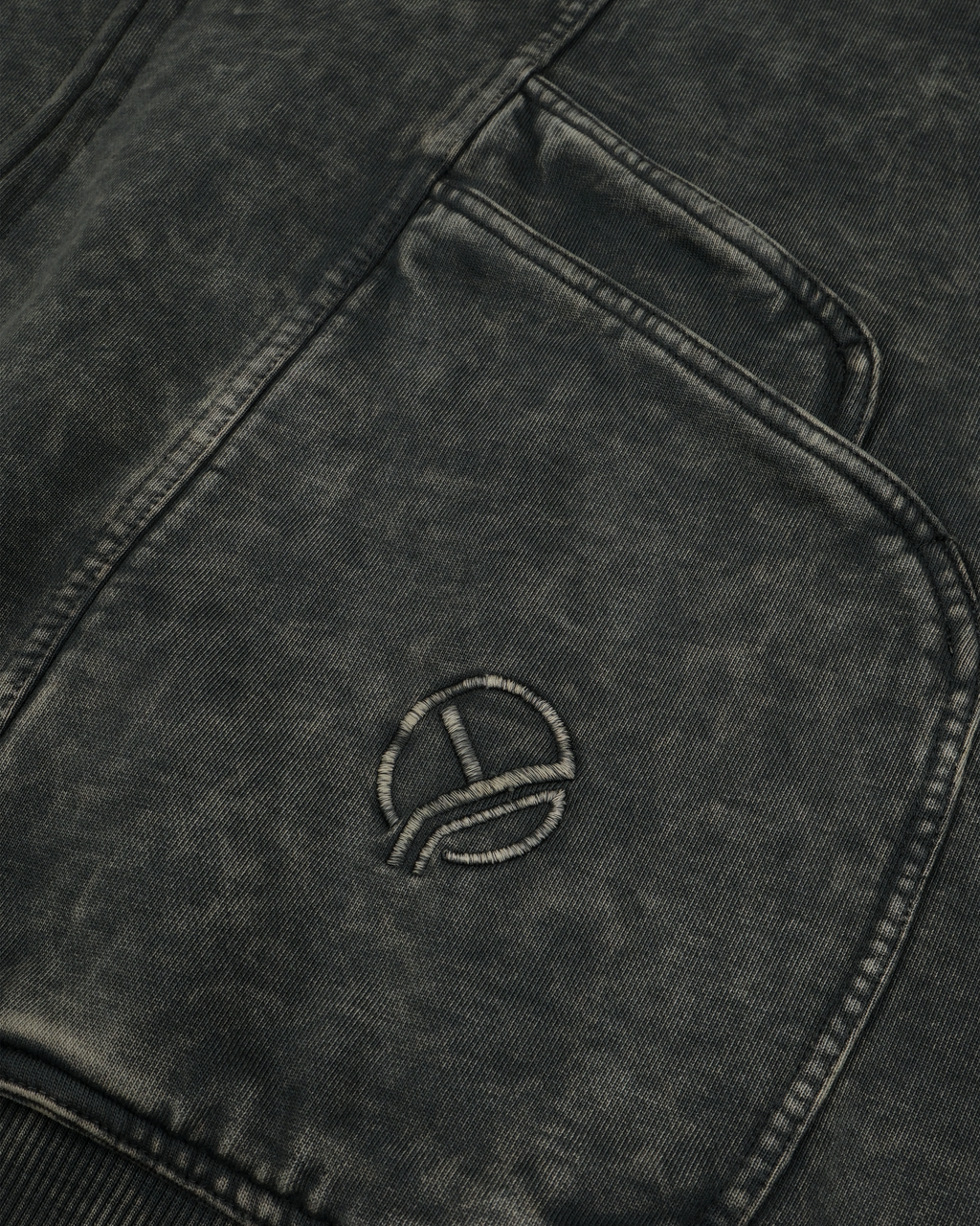 Nahaufnahme einer diagonalen Naht und der Taschenkante eines grauen Zip-Hoodies mit Washed-Effekt. Die Textur des Stoffes ist deutlich sichtbar, die Nahtlinien und der ausgewaschene Farbverlauf erzeugen eine