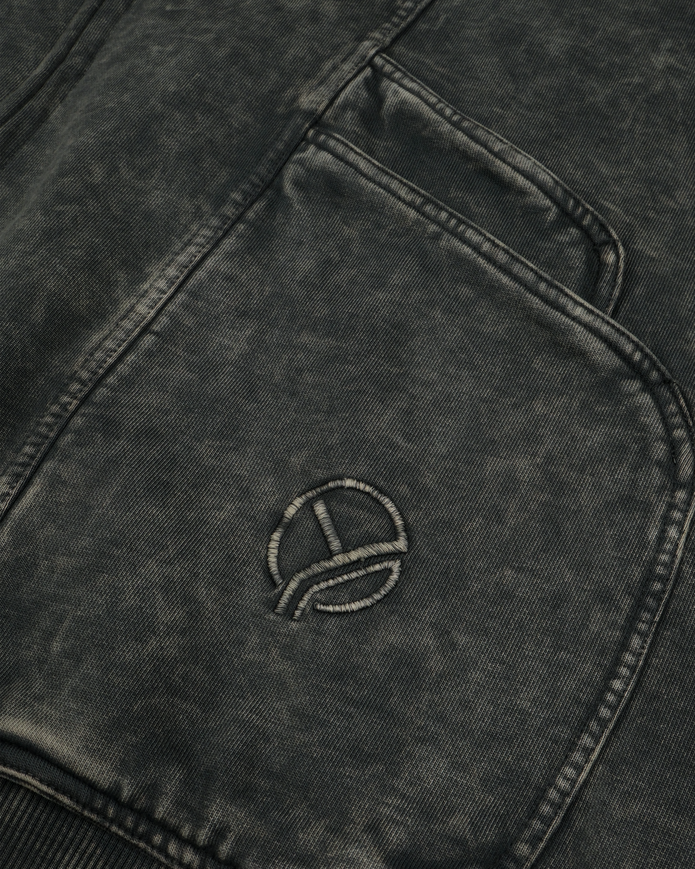 Nahaufnahme einer diagonalen Naht und der Taschenkante eines grauen Zip-Hoodies mit Washed-Effekt. Die Textur des Stoffes ist deutlich sichtbar, die Nahtlinien und der ausgewaschene Farbverlauf erzeugen eine