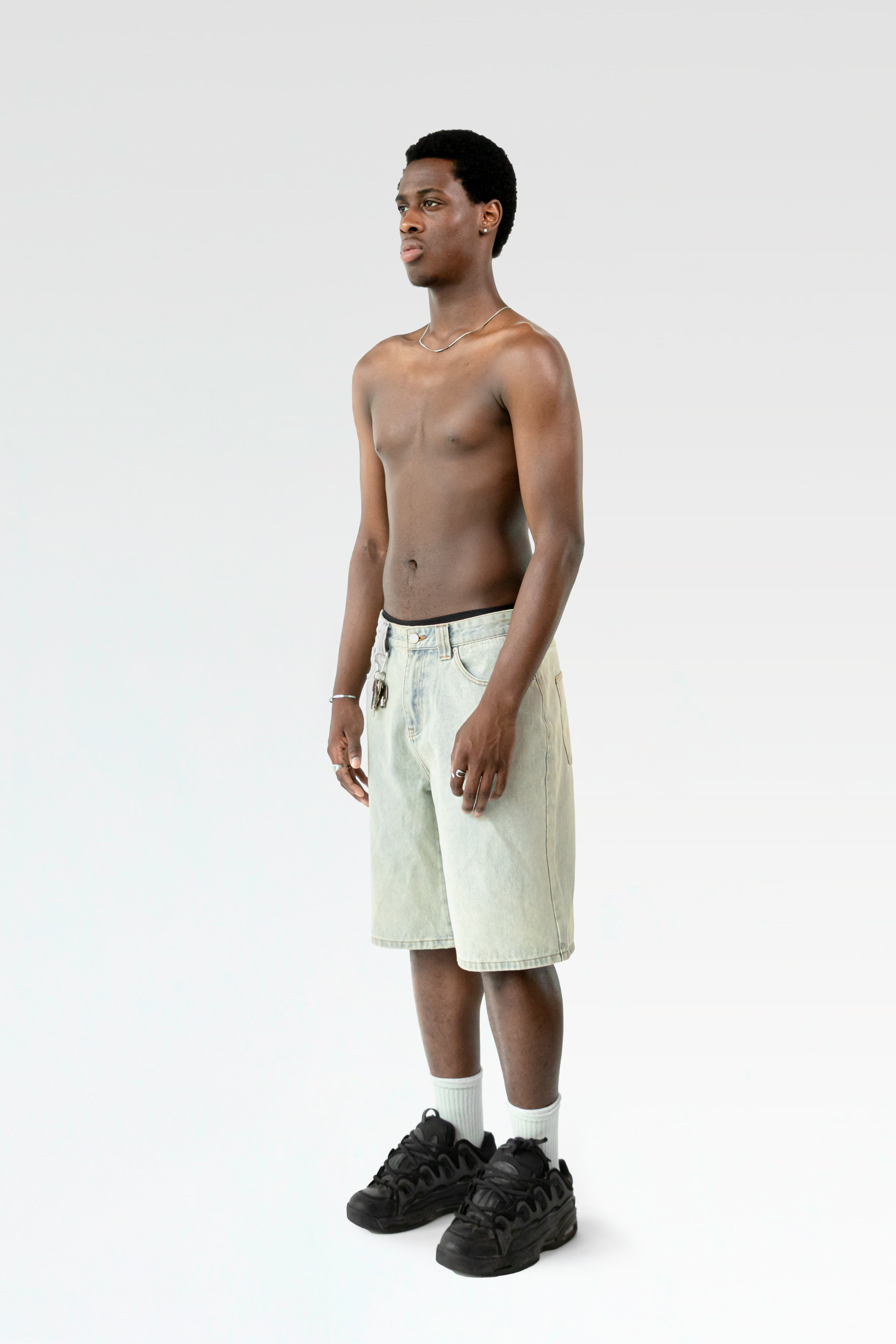 Seitliche Studioansicht der hellblauen Jorts an einer stehenden Person. Der gerade Schnitt und die gewaschene Optik des Denims sind erkennbar.