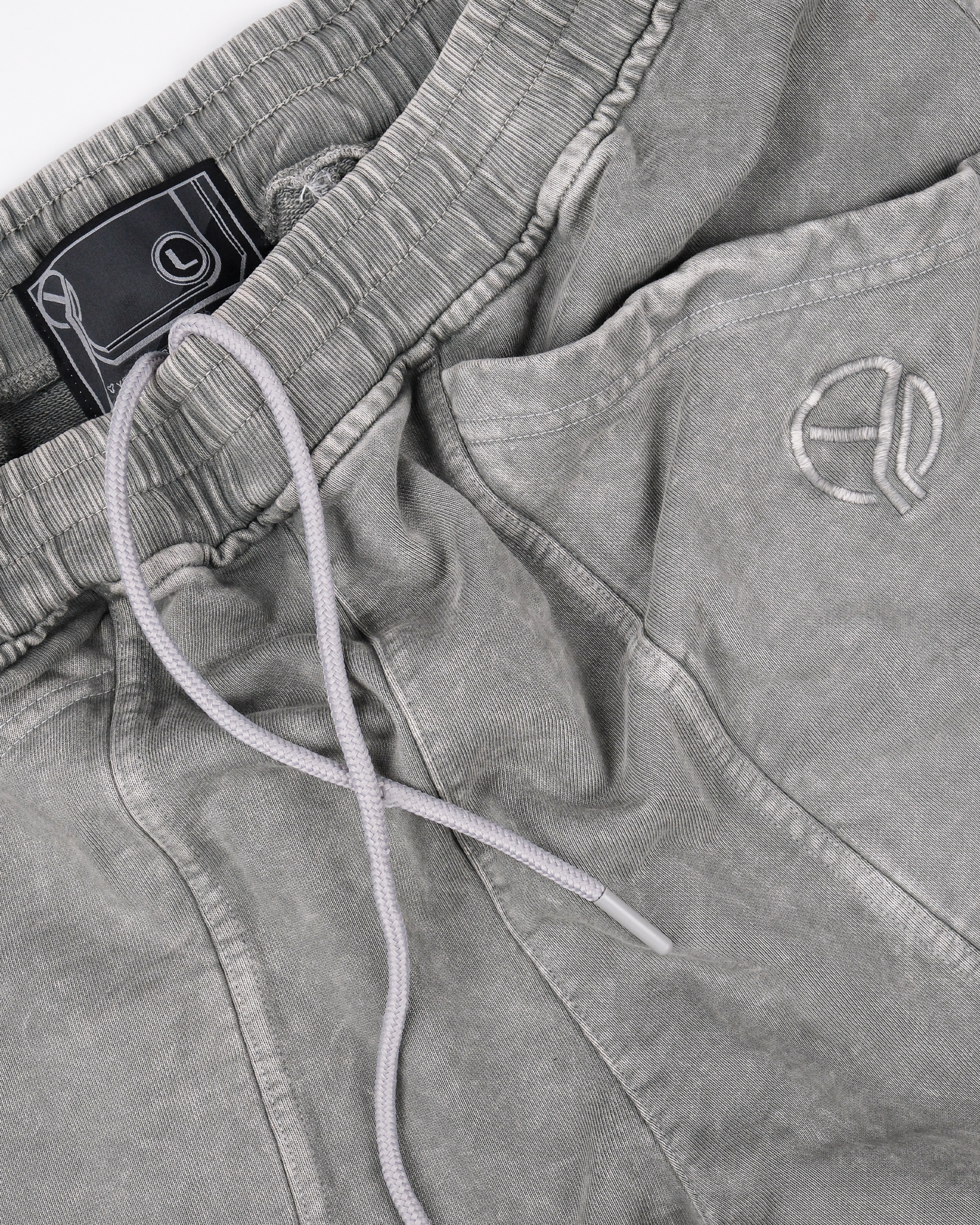 Nahaufnahme des oberen Teils einer grauen Sweatpants mit gewaschener Oberfläche, elastischem Bund mit Kordelzug und aufgesticktem YEU-Logo über der rechten Tasche.