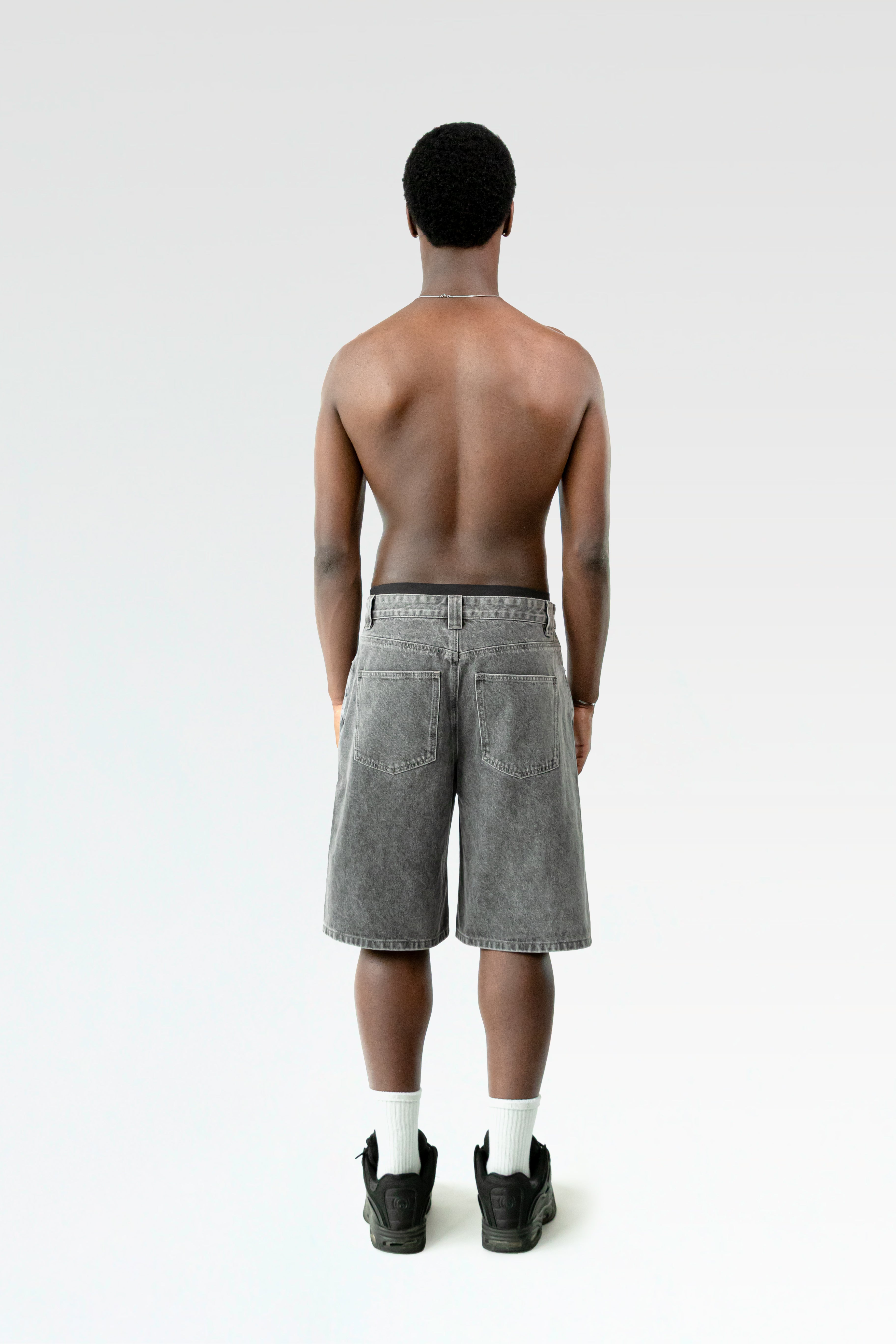 Rückansicht der hellgrau verwaschenen Bermuda-Shorts an einer stehenden Person. Die Hose hat zwei aufgesetzte Gesäßtaschen und einen geraden Saum.