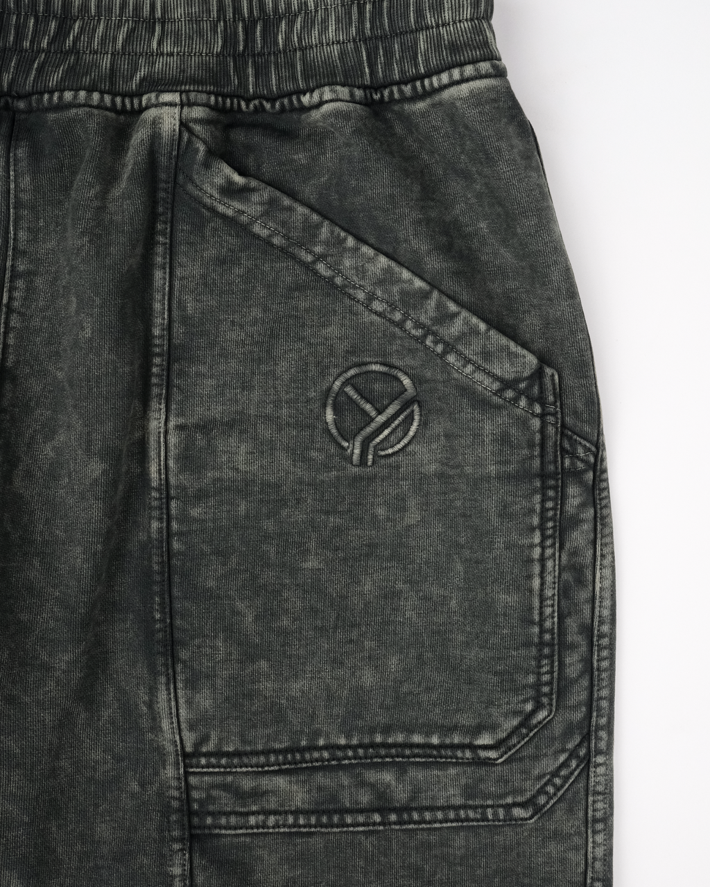 Vorderansicht der dunkelgrünen Sweatpants mit zwei aufgesetzten Gesäßtaschen, einer Logo-Stickerei auf der rechten Seite und dynamisch geschwungenen Teilungsnähten an beiden Hosenbeinen. Die Hose hat eine breite, gerade Beinform und ein elastisches Bündchen.