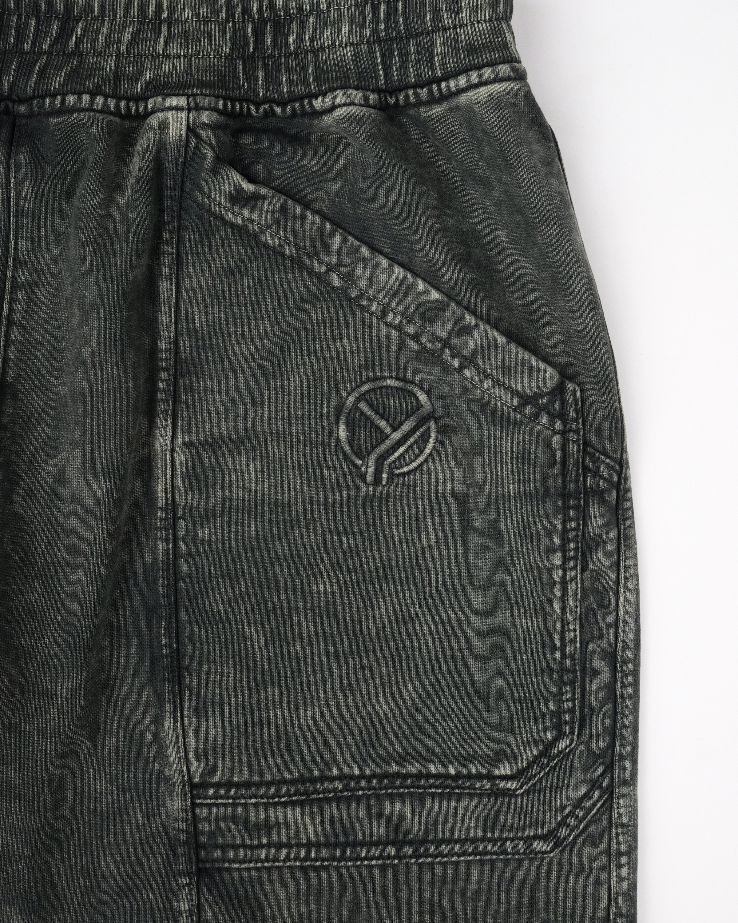 Vorderansicht der dunkelgrünen Sweatpants mit zwei aufgesetzten Gesäßtaschen, einer Logo-Stickerei auf der rechten Seite und dynamisch geschwungenen Teilungsnähten an beiden Hosenbeinen. Die Hose hat eine breite, gerade Beinform und ein elastisches Bündchen.