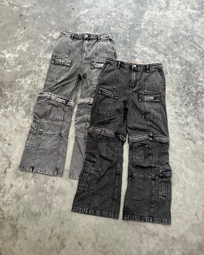 Zwei Cargo-Hosen aus verwaschenem Denim liegen flach auf grauem Untergrund. Links ein Modell in Hellgrau, rechts ein Modell in Schwarz. Beide Hosen zeigen mehrere Taschen, Teilungsnähte und Logos auf den Oberschenkeltaschen.