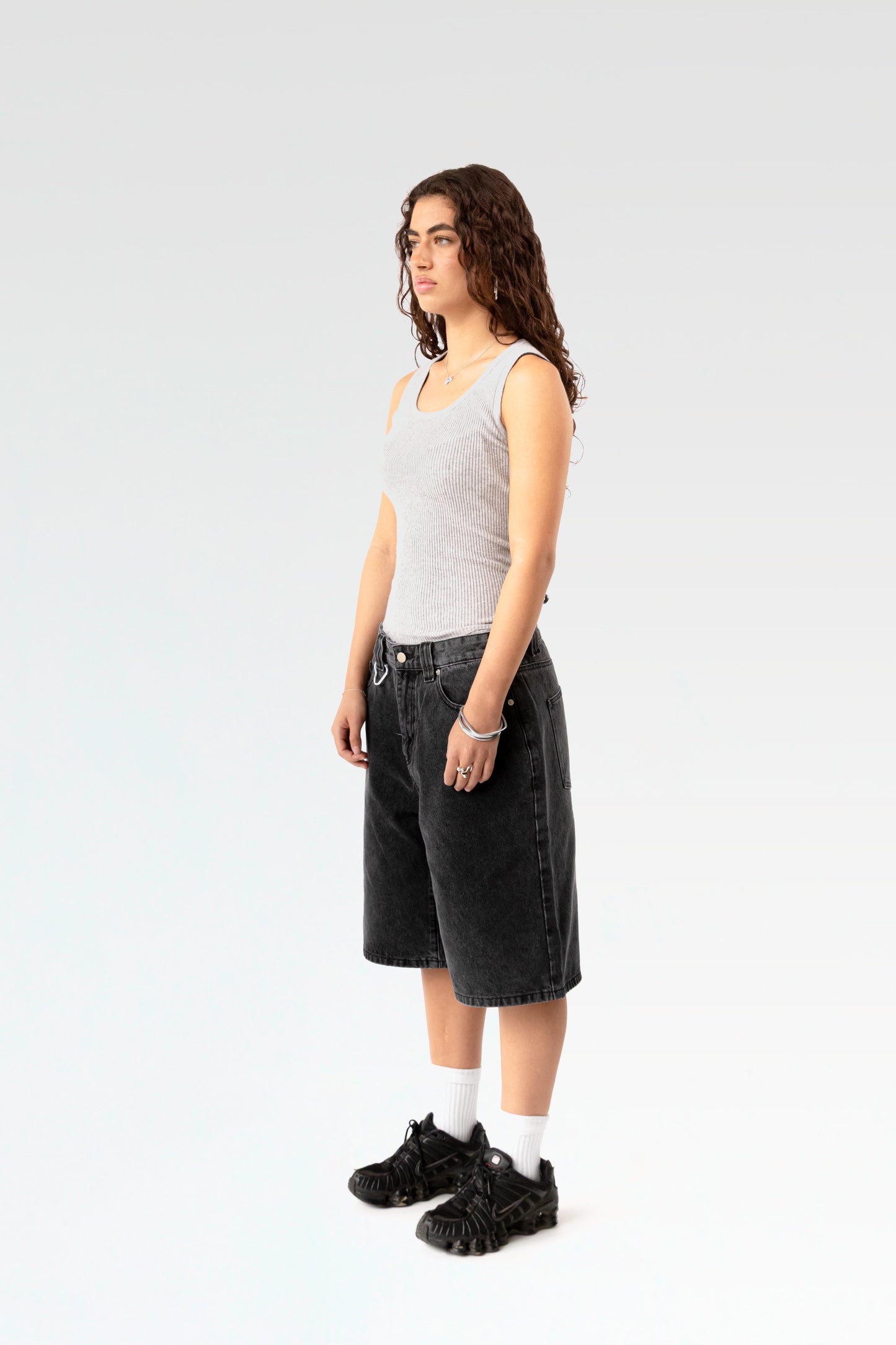 Schräg seitliche Ansicht der schwarzen Bermuda-Shorts an einer stehenden Person. Die weite Beinform und die klassische 5-Pocket-Optik sind gut sichtbar.