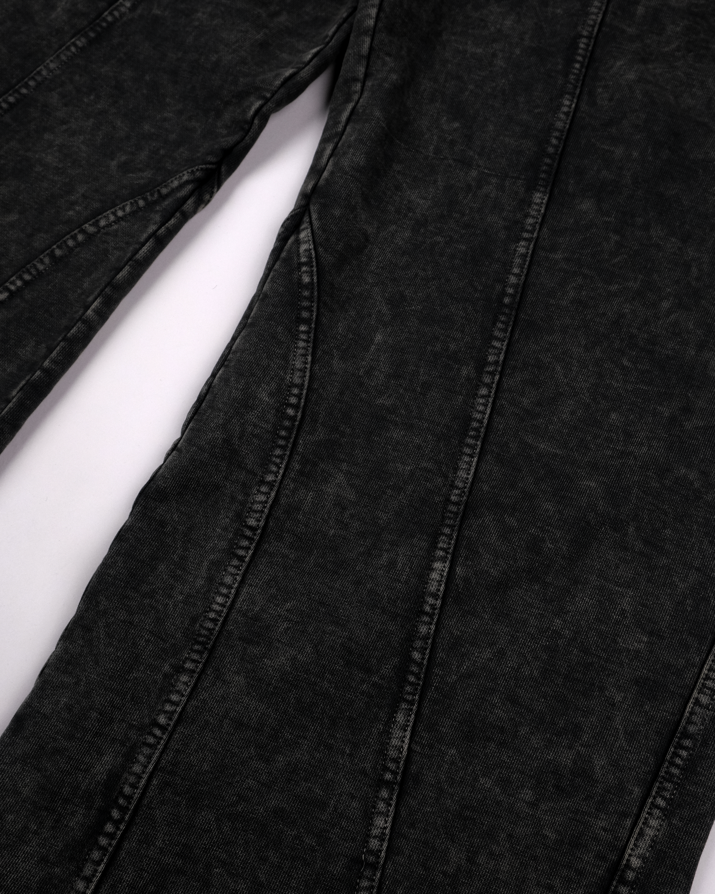Detailaufnahme der Hosenbeine mit Fokus auf die gewaschenen Strukturen des Stoffes und die markant abgesetzten, geschwungenen Ziernähte. Die Materialstruktur ist deutlich sichtbar, mit helleren Waschungsspuren entlang der Nahtlinien.

