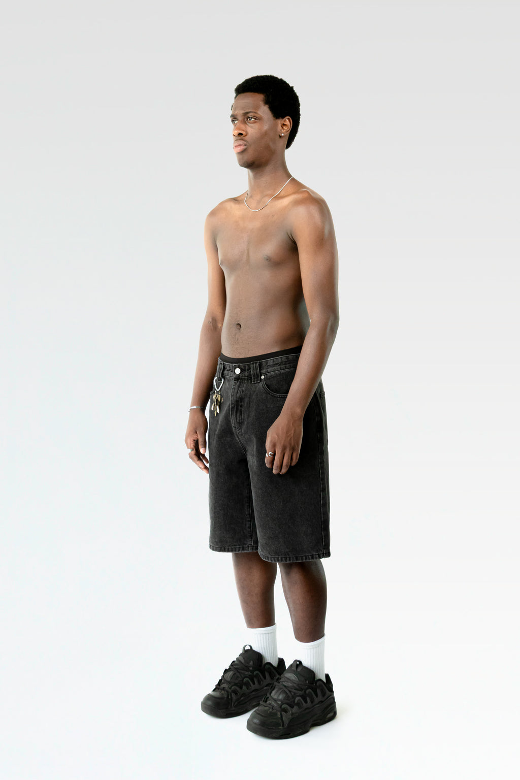 Seitliche Studioansicht der schwarzen Jorts an einer stehenden Person. Der gerade Schnitt und das ausgewaschene Schwarz der Hose sind erkennbar.