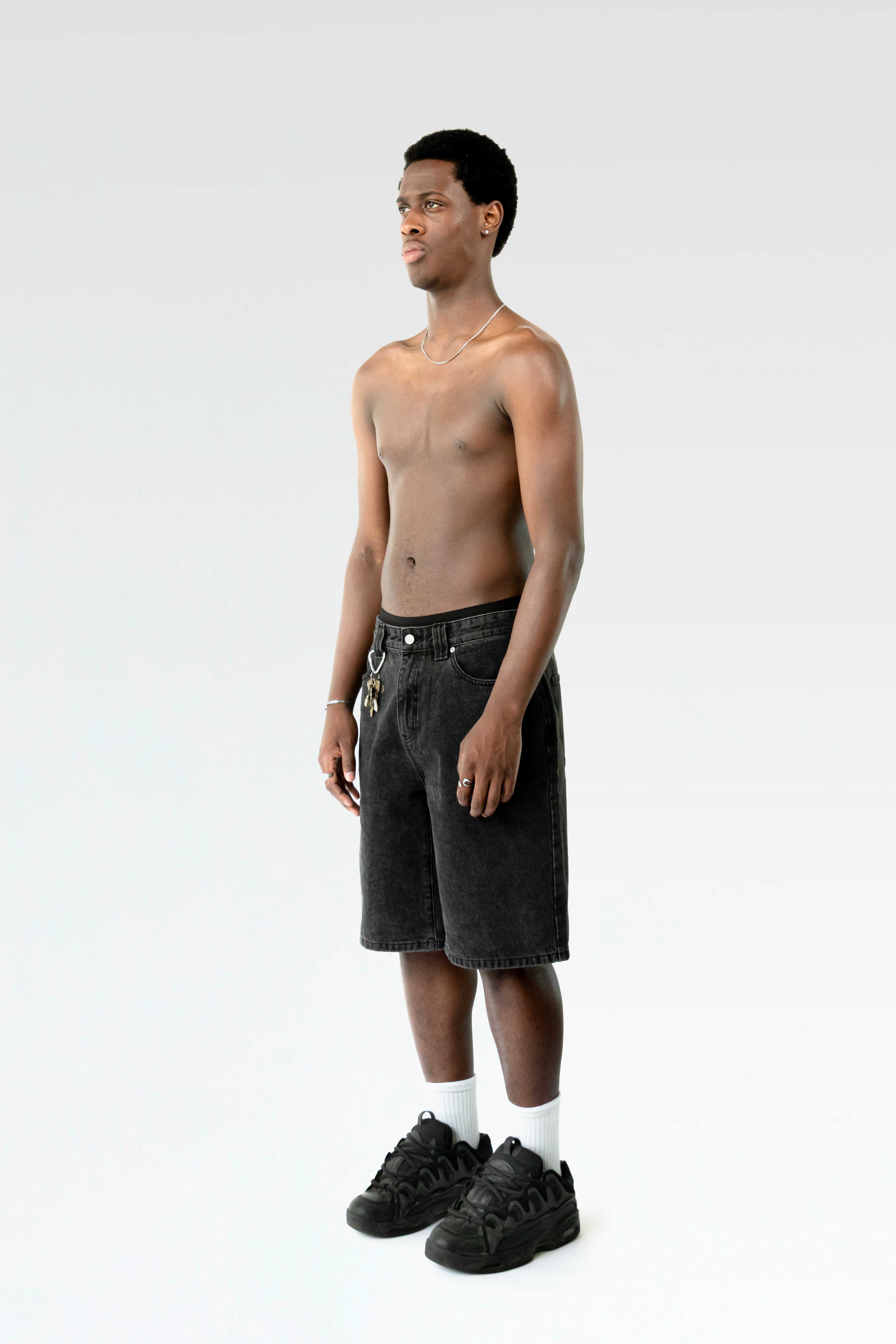 Seitliche Studioansicht der schwarzen Jorts an einer stehenden Person. Der gerade Schnitt und das ausgewaschene Schwarz der Hose sind erkennbar.