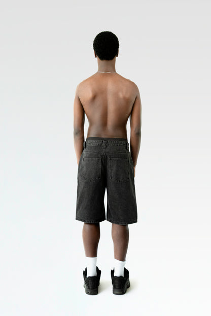 Rückansicht der schwarzen Bermuda-Shorts an einer stehenden Person. Die Hose hat zwei aufgesetzte Gesäßtaschen und einen geraden Saum.