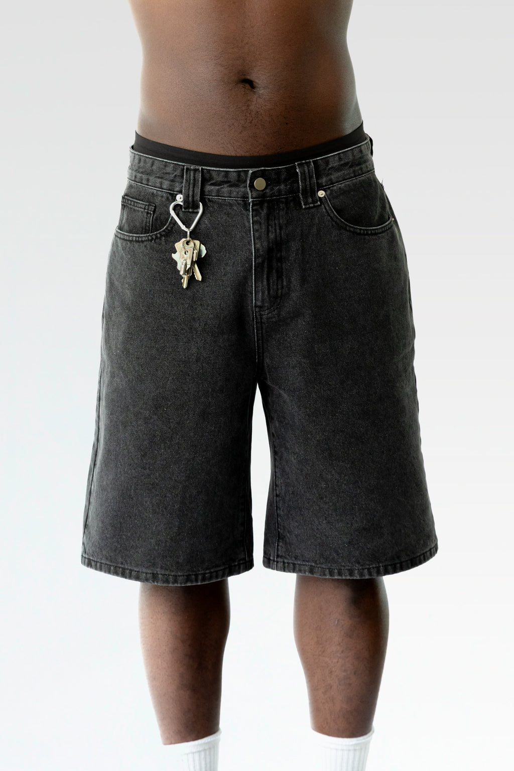 Nahaufnahme der schwarzen Bermuda-Shorts im getragenen Zustand, mit Fokus auf den Karabinerhaken samt Schlüsselbund an der Gürtelschlaufe.
