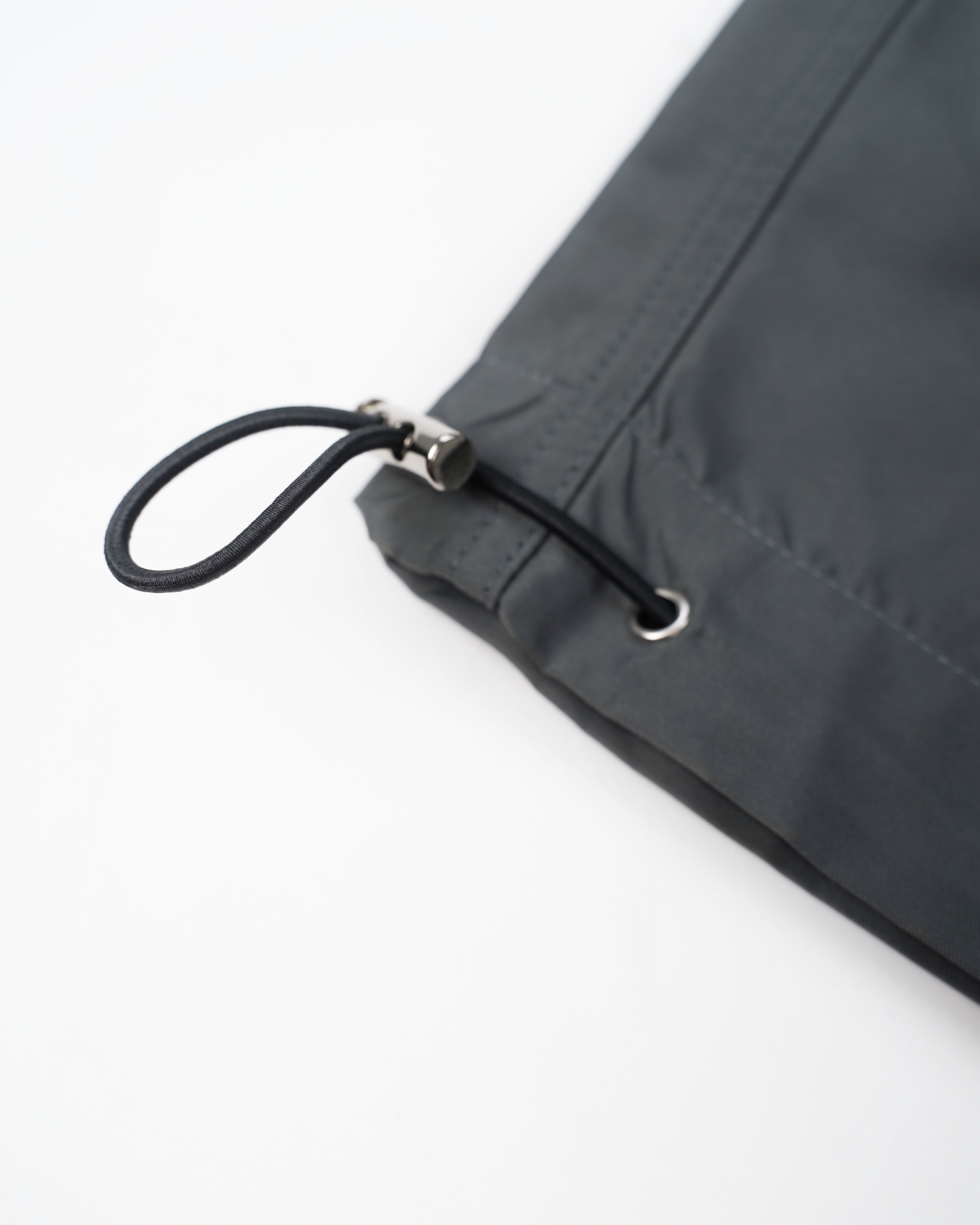 Nahaufnahme des Beinabschlusses der Hose mit integriertem, schwarzem Gummizug und silbernem Stopper. Der Kordelzug ist durch silberne Ösen geführt und dient zur individuellen Weitenregulierung.

