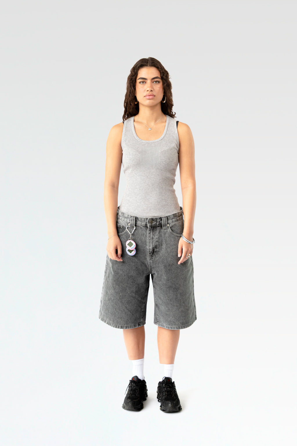 Frontale Studioaufnahme einer hellgrau verwaschenen Denim-Bermuda-Shorts an einer stehenden Person. Die Shorts ist knielang geschnitten und hat eine weite Passform sowie einen silbernen Karabinerhaken an der Gürtelschlaufe.
