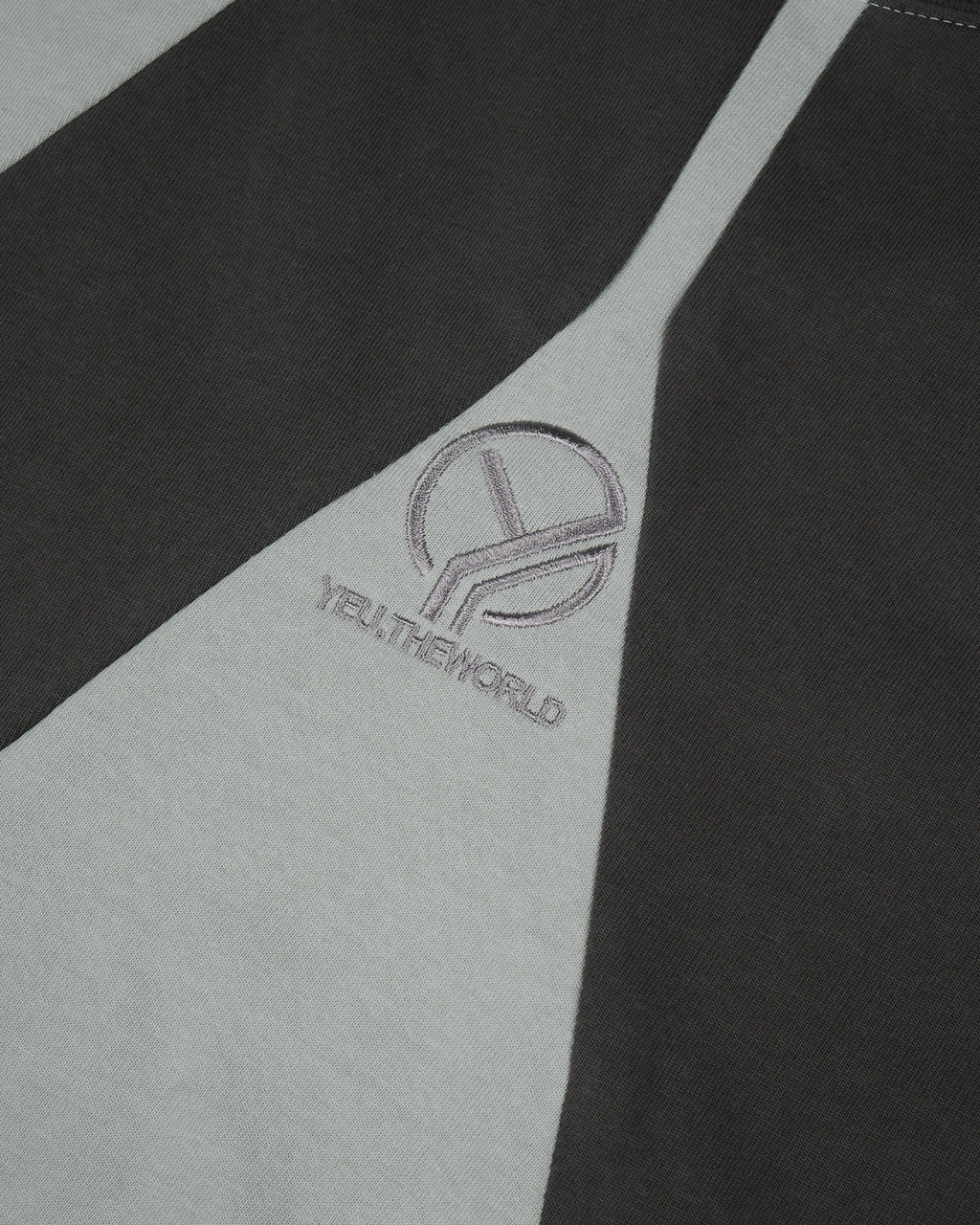 Nahansicht eines zweifarbigen T-Shirts in dunklem Graugrün und Schwarz mit mittig platzierter, fein gestickter „YEU.THEWORLD“-Wort-Bild-Marke in Grau.