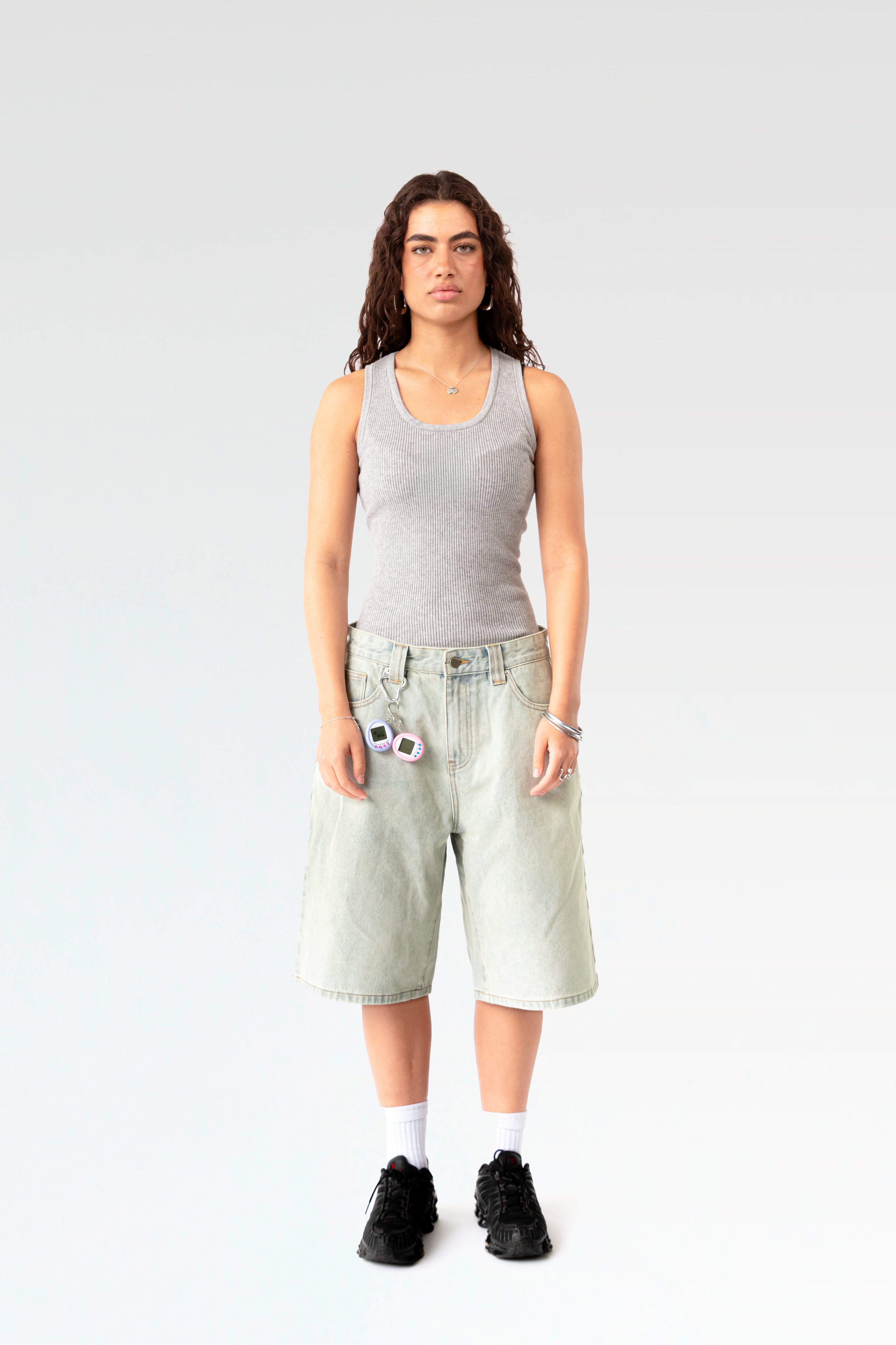 Frontale Studioaufnahme einer hellblauen Denim-Bermuda-Shorts an einer stehenden Person. Die Shorts ist knielang geschnitten und hat eine weite Passform sowie einen silbernen Karabinerhaken an der Gürtelschlaufe.