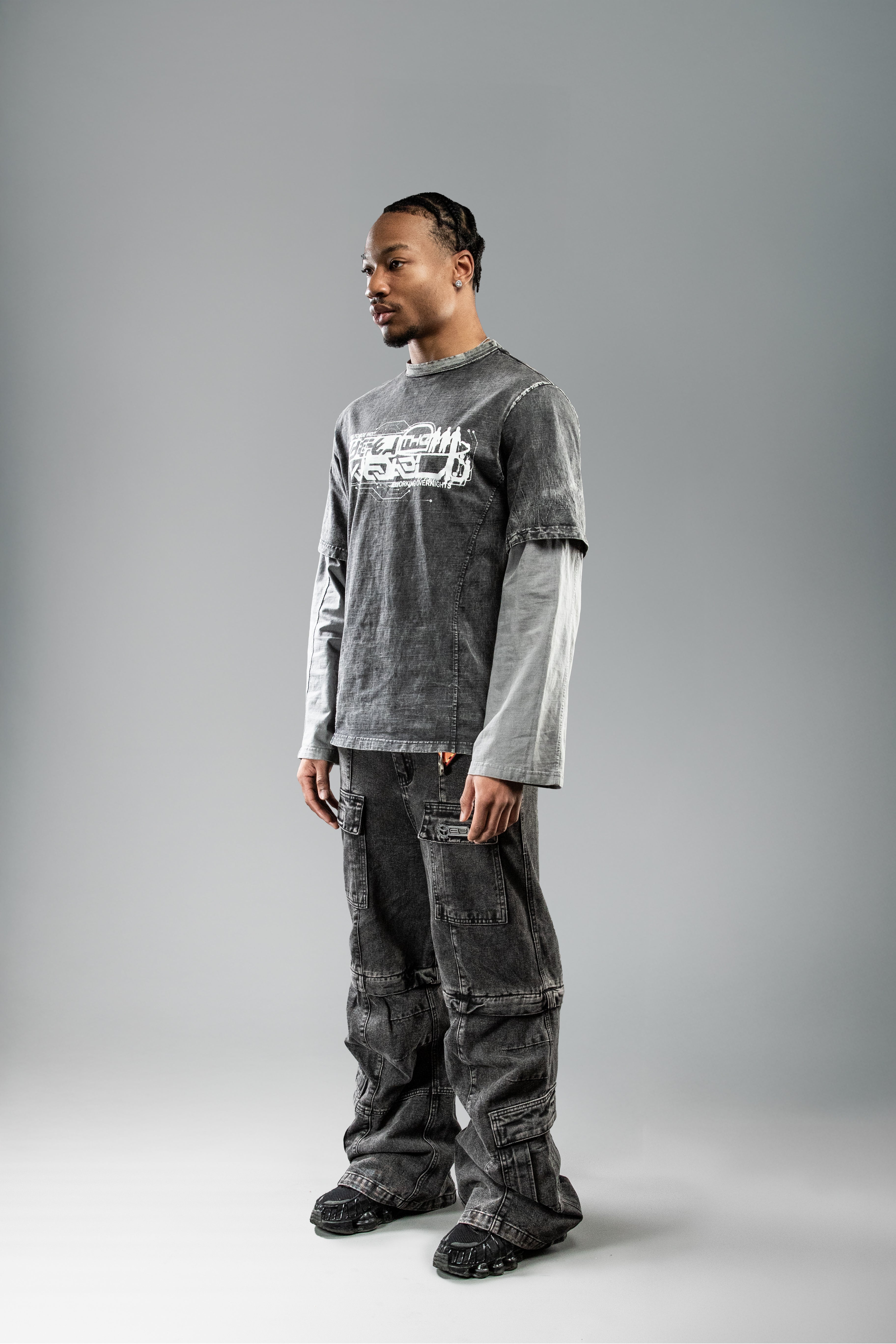 Seitliche Studioaufnahme des schwarzen Layering-Shirts mit Oversleeves. Der Frontprint auf der Brust ist nur teilweise sichtbar. Die langen, grauen Ärmel und die Waschung des Hauptstoffs kommen gut zur Geltung