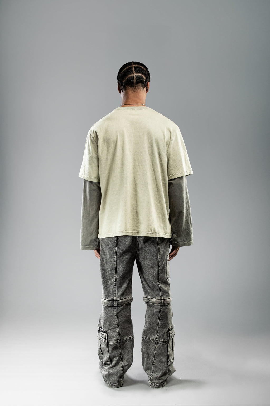 Rückansicht eines Models im olivgrünen Layer-Shirt mit dunklen Ärmeln. Die Rückseite ist unbedruckt, der gerade Schnitt und die lockere Passform sind gut erkennbar.
