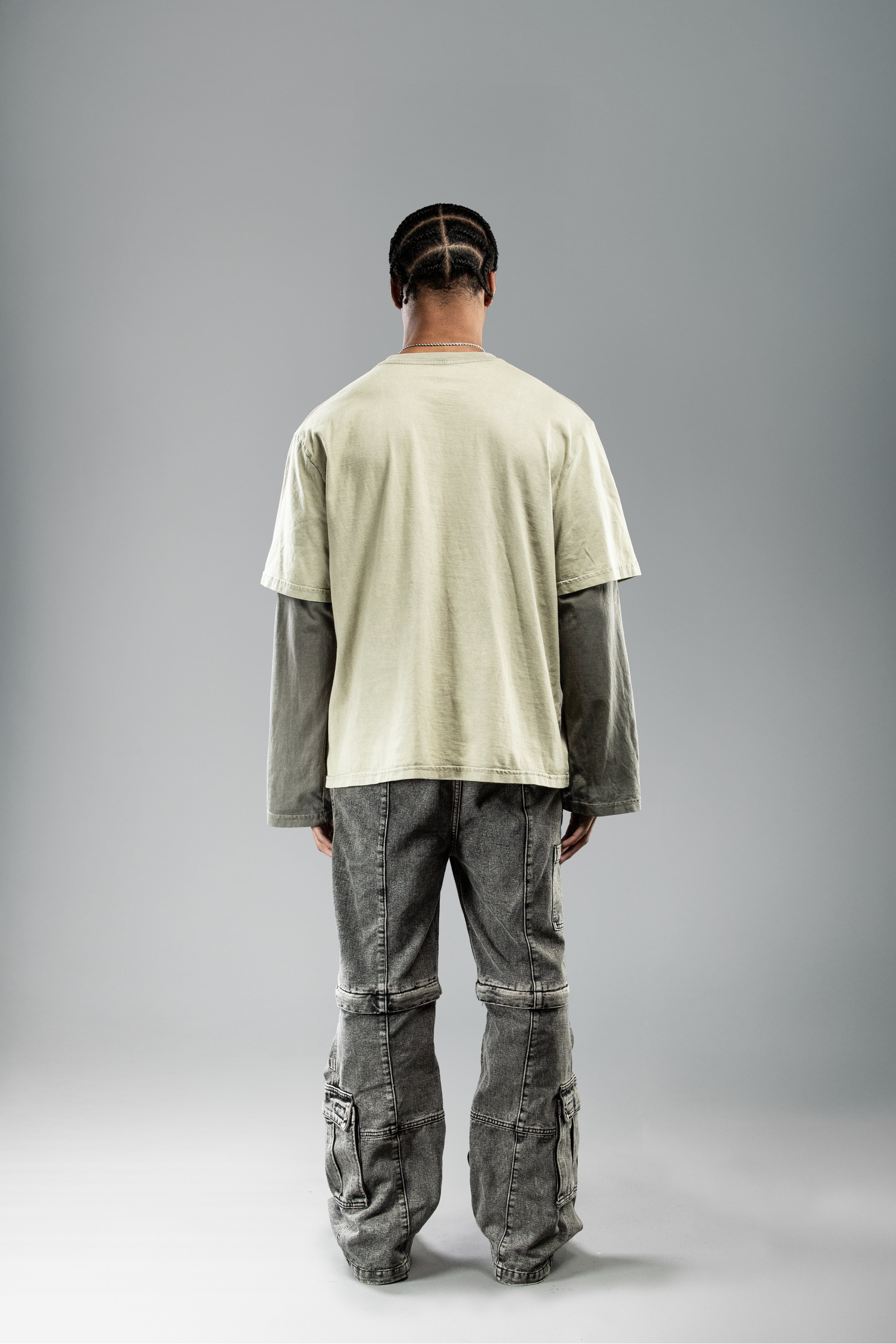 Rückansicht eines Models im olivgrünen Layer-Shirt mit dunklen Ärmeln. Die Rückseite ist unbedruckt, der gerade Schnitt und die lockere Passform sind gut erkennbar.
