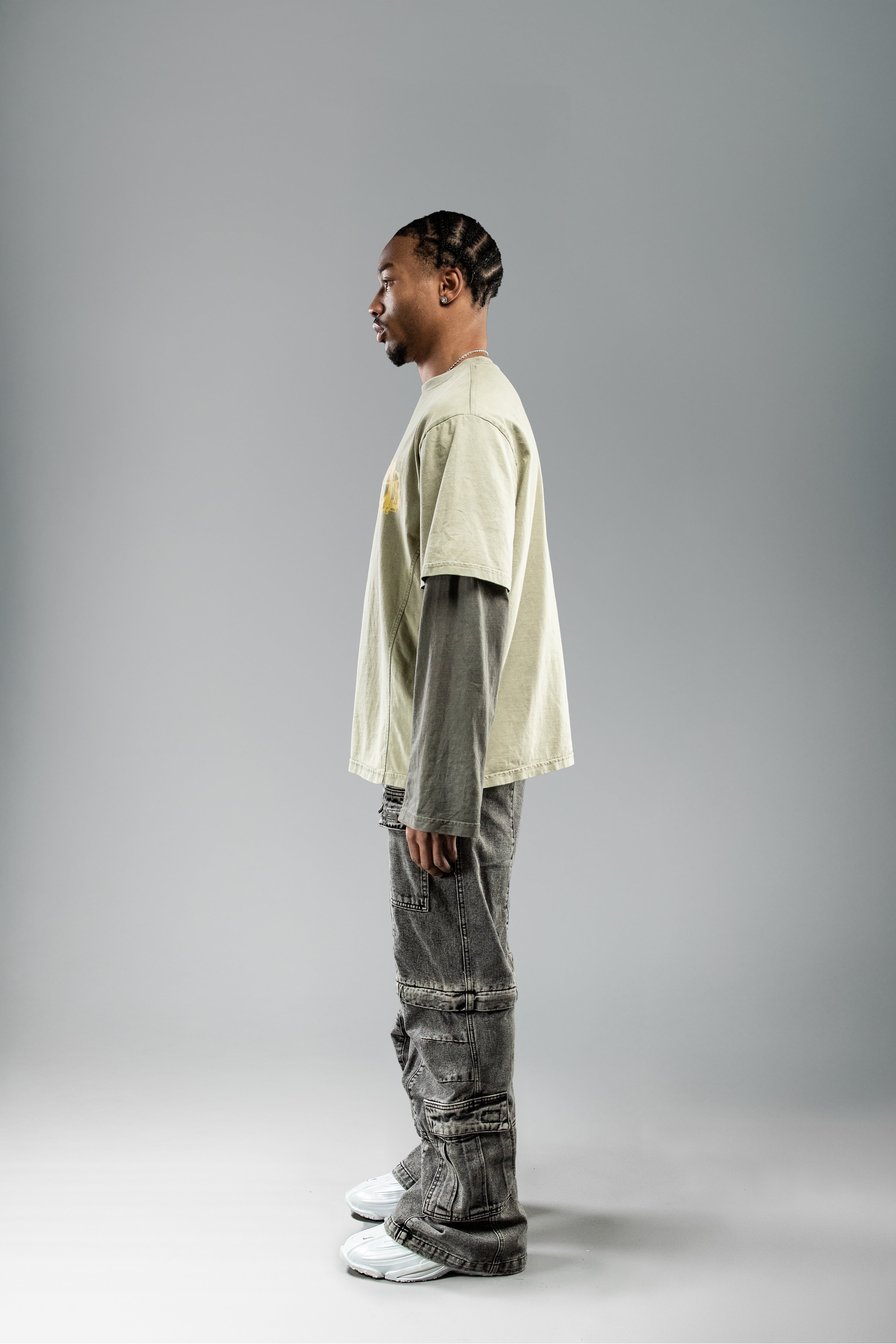 Seitliche Studioaufnahme eines stehenden Models mit olivgrünem Layer-Shirt. Der lockere Schnitt und die unterschiedlich gefärbten Ärmel sind gut sichtbar.