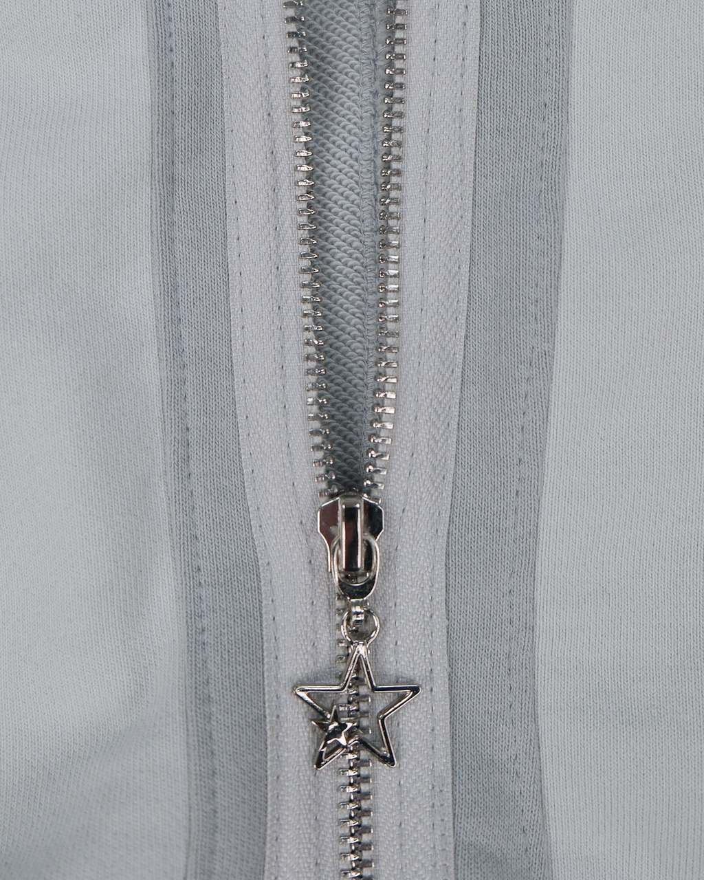 Nahaufnahme des Reißverschlusses am hellgrauen Hoodie mit silbernem Sternanhänger als Zipper-Detail.