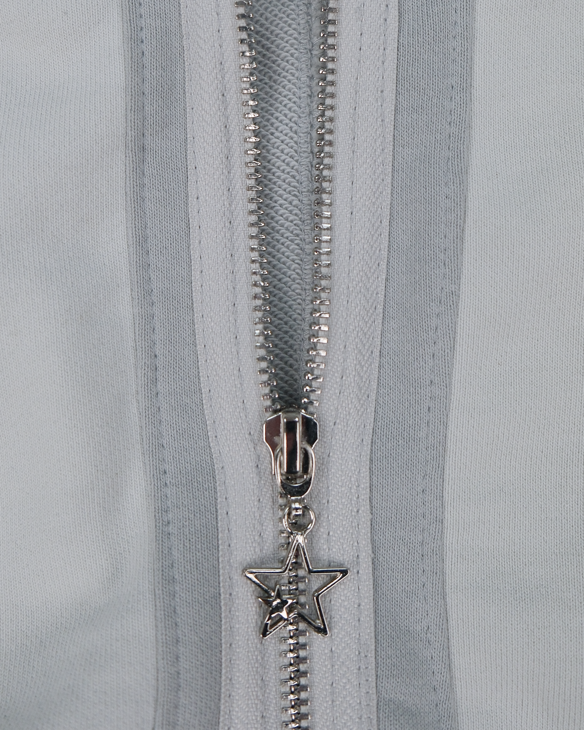 Nahaufnahme des Reißverschlusses am hellgrauen Hoodie mit silbernem Sternanhänger als Zipper-Detail.
