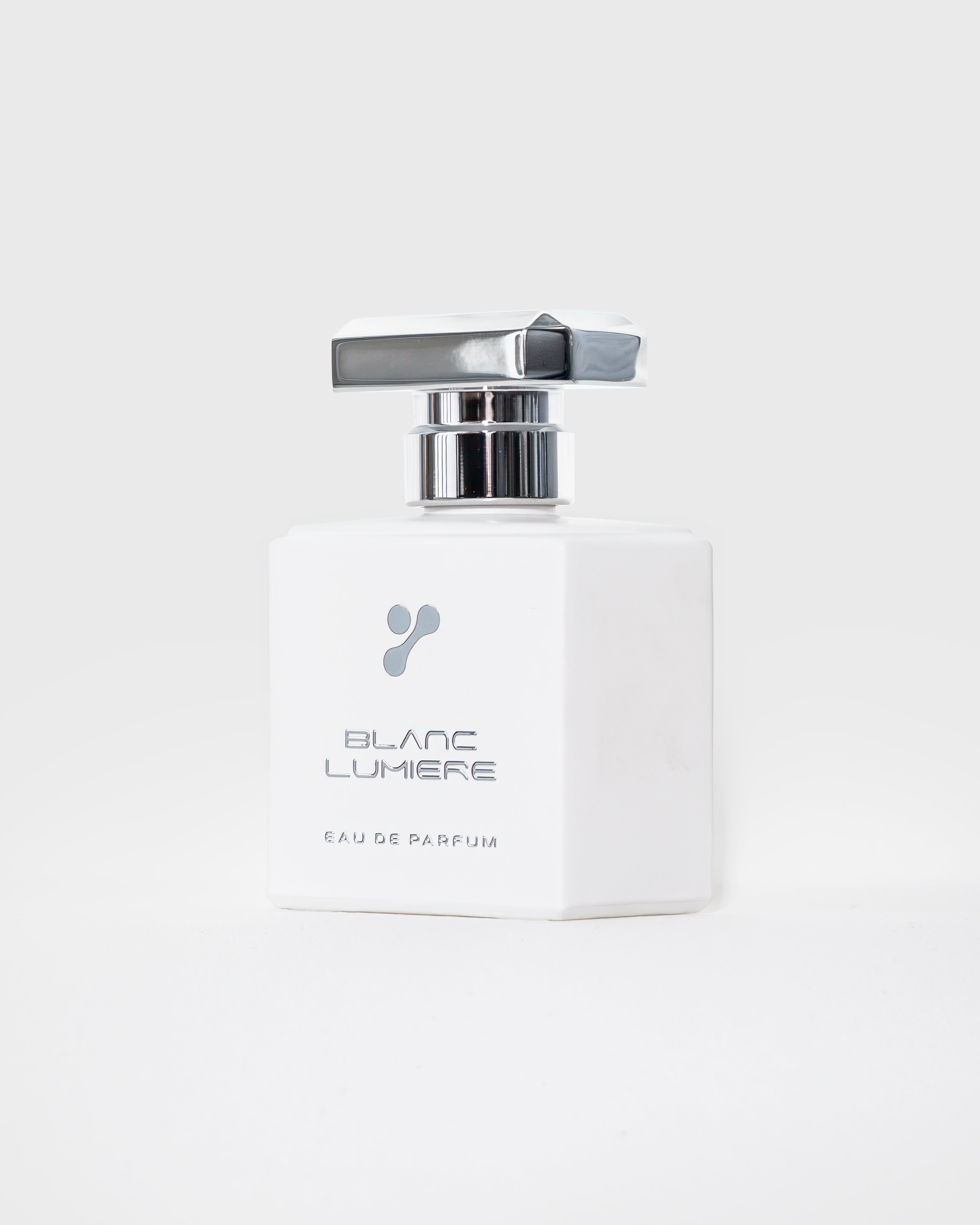 Weißer Parfumflakon schräg von vorn mit Logo und Schriftzug „BLANC LUMIERE – Eau de Parfum“, silberner Deckel.