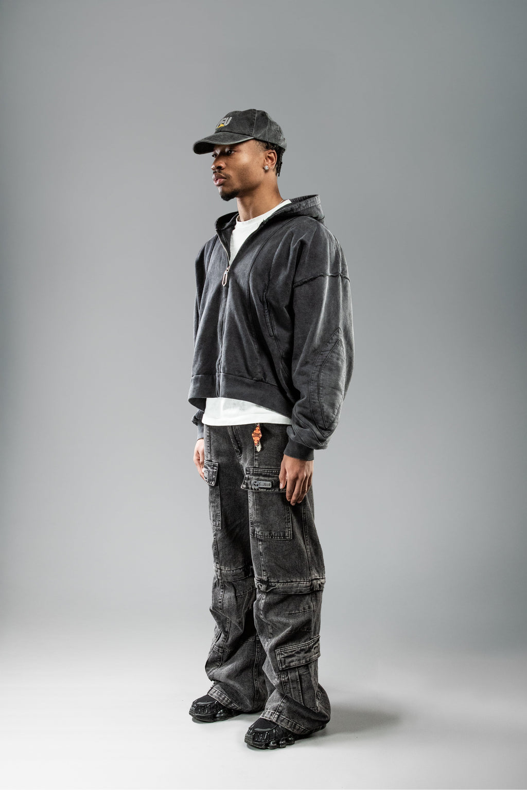 Schwarzer Zip-Hoodie leicht seitlich getragen. Die geformten Teilungsnähte auf Brust und Schulter heben sich durch die Waschung deutlich ab. Die Kapuze liegt nach hinten gefaltet.