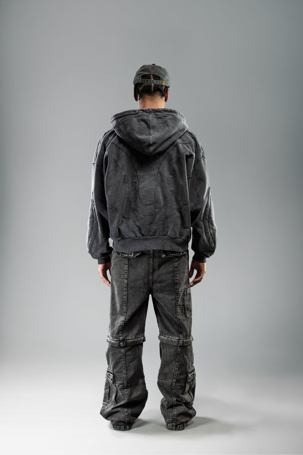 Schwarzer Zip-Hoodie von hinten getragen, Kapuze liegt locker auf dem Rücken. Sichtbar ist die geschwungene Nahtstruktur im oberen Rückenbereich, die einen organischen Verlauf bildet.