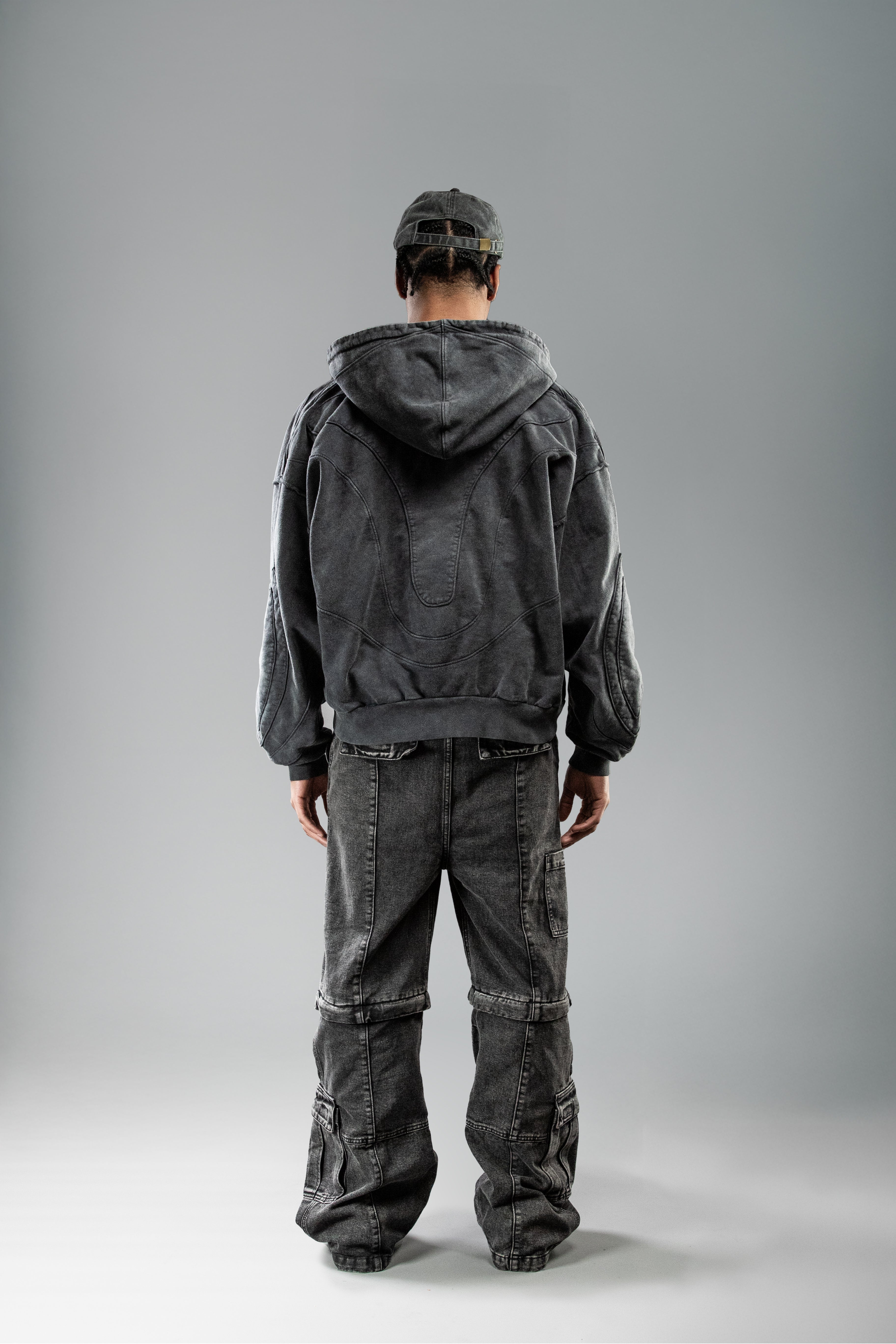 Schwarzer Zip-Hoodie von hinten getragen, Kapuze liegt locker auf dem Rücken. Sichtbar ist die geschwungene Nahtstruktur im oberen Rückenbereich, die einen organischen Verlauf bildet.