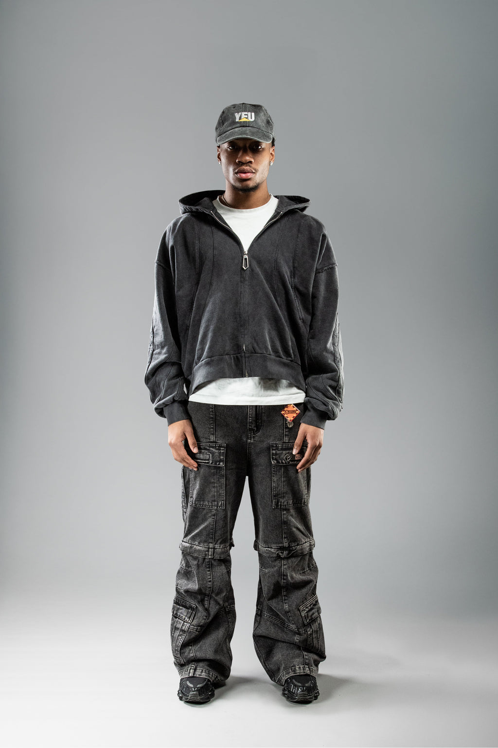 Schwarzer Zip-Hoodie an Person frontal getragen. Der Reißverschluss ist geschlossen, der Hoodie zeigt eine leicht ausgewaschene Struktur. Der Saum endet oberhalb der Hüfte, der Sitz ist locker und kastig.