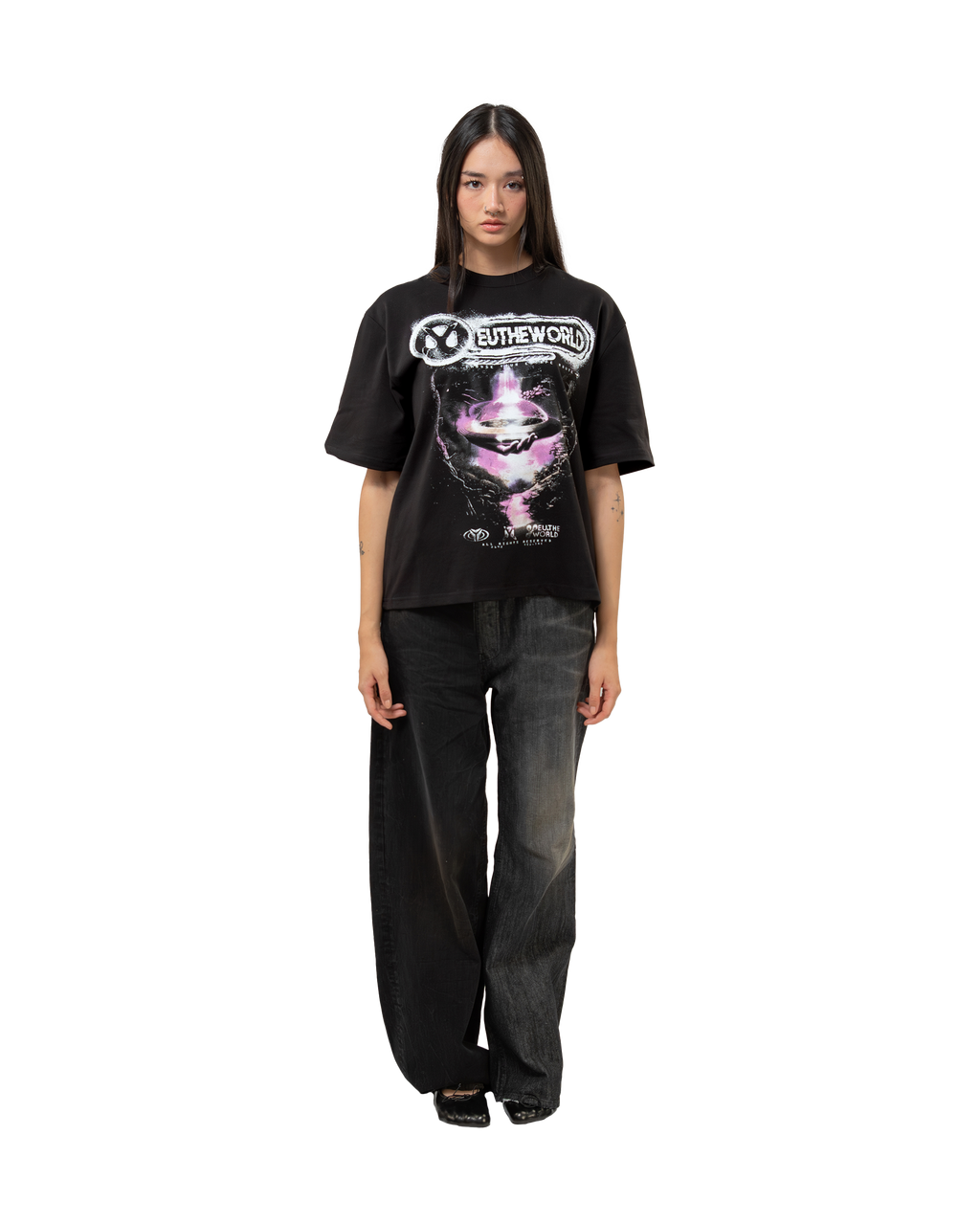 Frontalansicht des schwarzen T-Shirts an einer Person. Das T-Shirt hat eine lockere Passform und zeigt mittig das große, kontrastreiche Printmotiv mit UFO, „EUTHEWORLD“-Schriftzug und leuchtenden Farbeffekten in Rosa und Weiß. Das Shirt endet knapp über der Hüfte und wird zu einer Jeans kombiniert.