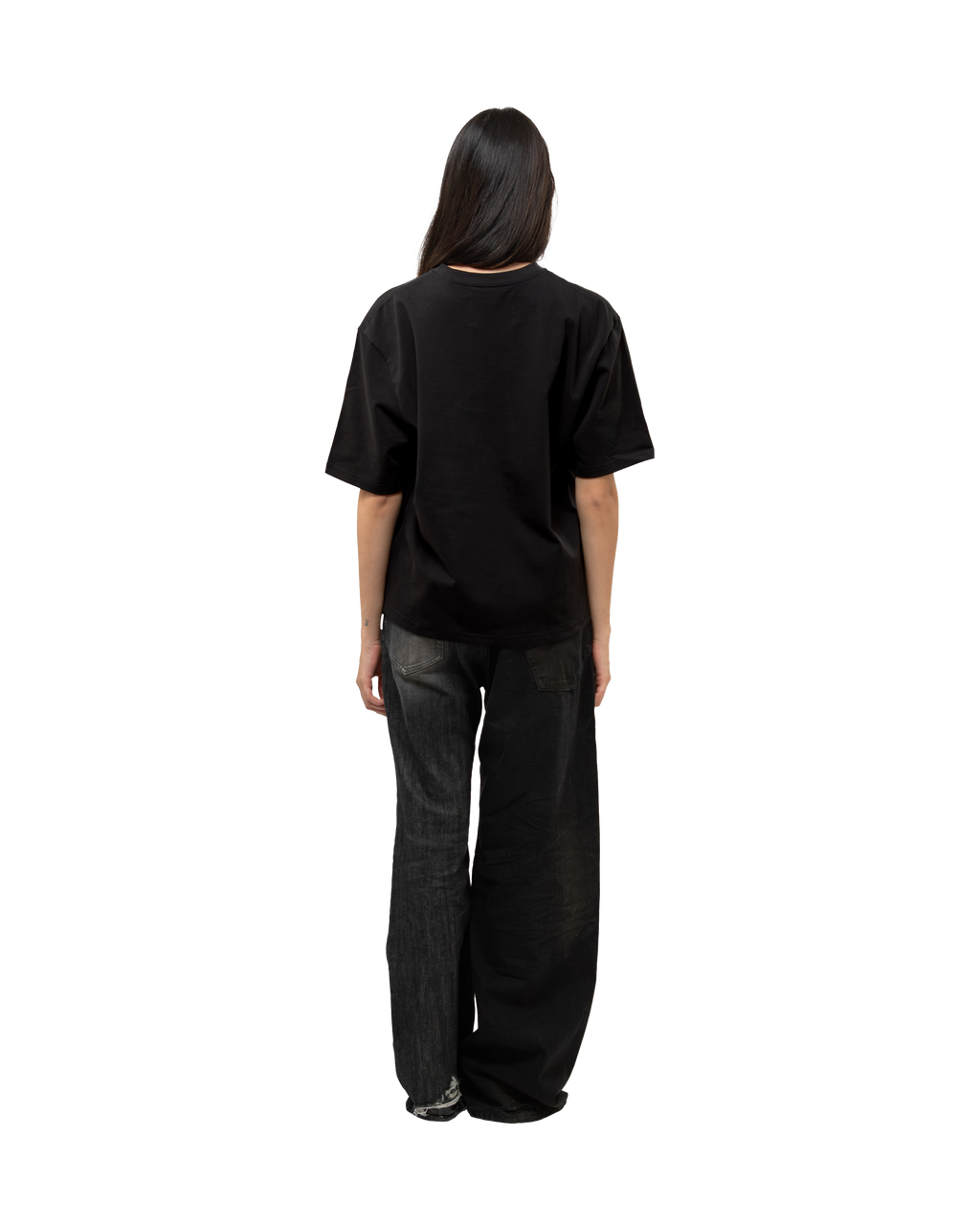 Rückansicht einer stehenden Person im schwarzen T-Shirt. Die Rückseite des Shirts ist schlicht und unbedruckt. Getragen wird es locker fallend über einer weit geschnittenen Jeans mit ausgeblichener Waschung.
