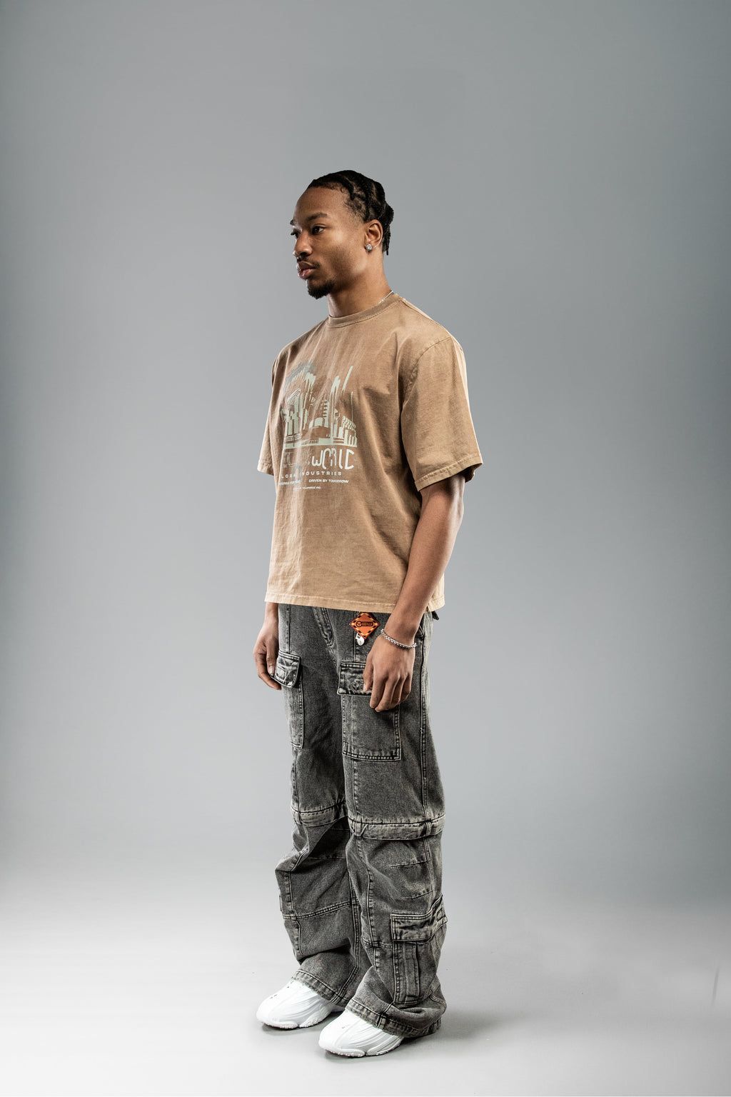 Braunes T-Shirt mit industriellem Frontprint, getragen in halber Seitenansicht. Der Print zeigt stilisierte Gebäude und Zahnräder in Beige und Hellblau.