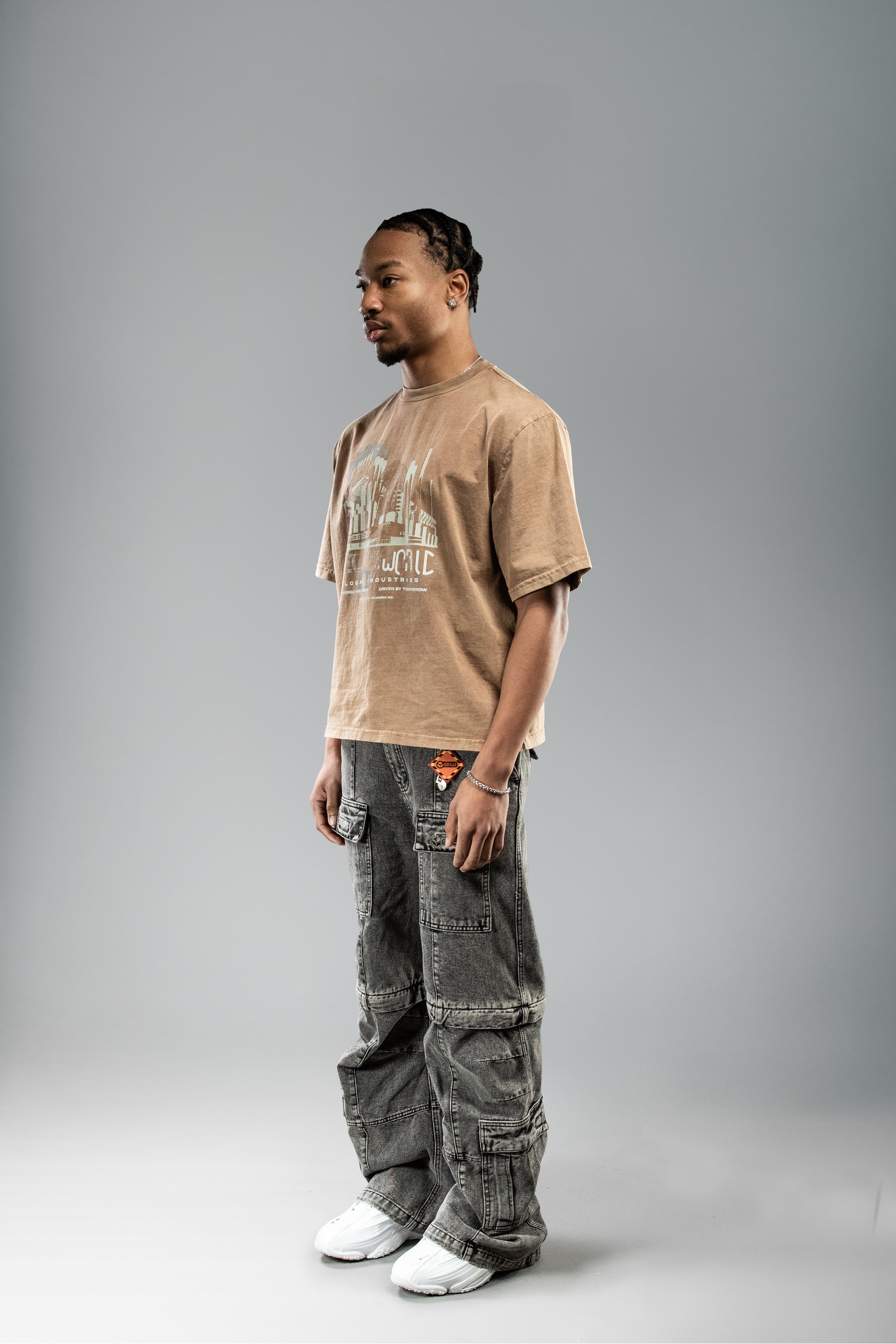 Braunes T-Shirt mit industriellem Frontprint, getragen in halber Seitenansicht. Der Print zeigt stilisierte Gebäude und Zahnräder in Beige und Hellblau.