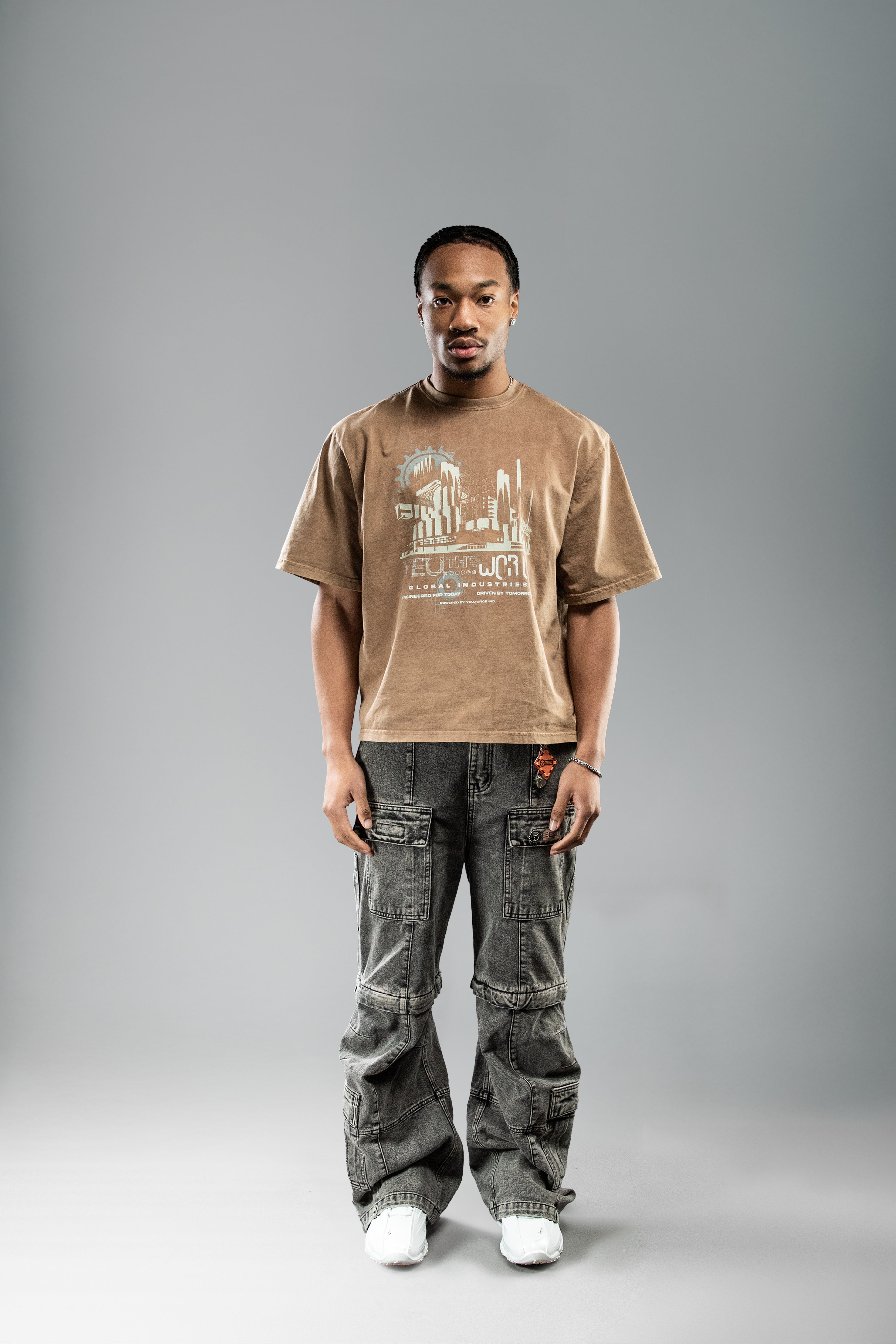 Frontalansicht eines braunen T-Shirts mit hellem Stadtgrafik-Print auf der Brust. Getragen zu einer verwaschenen Cargohose mit breitem Bein.