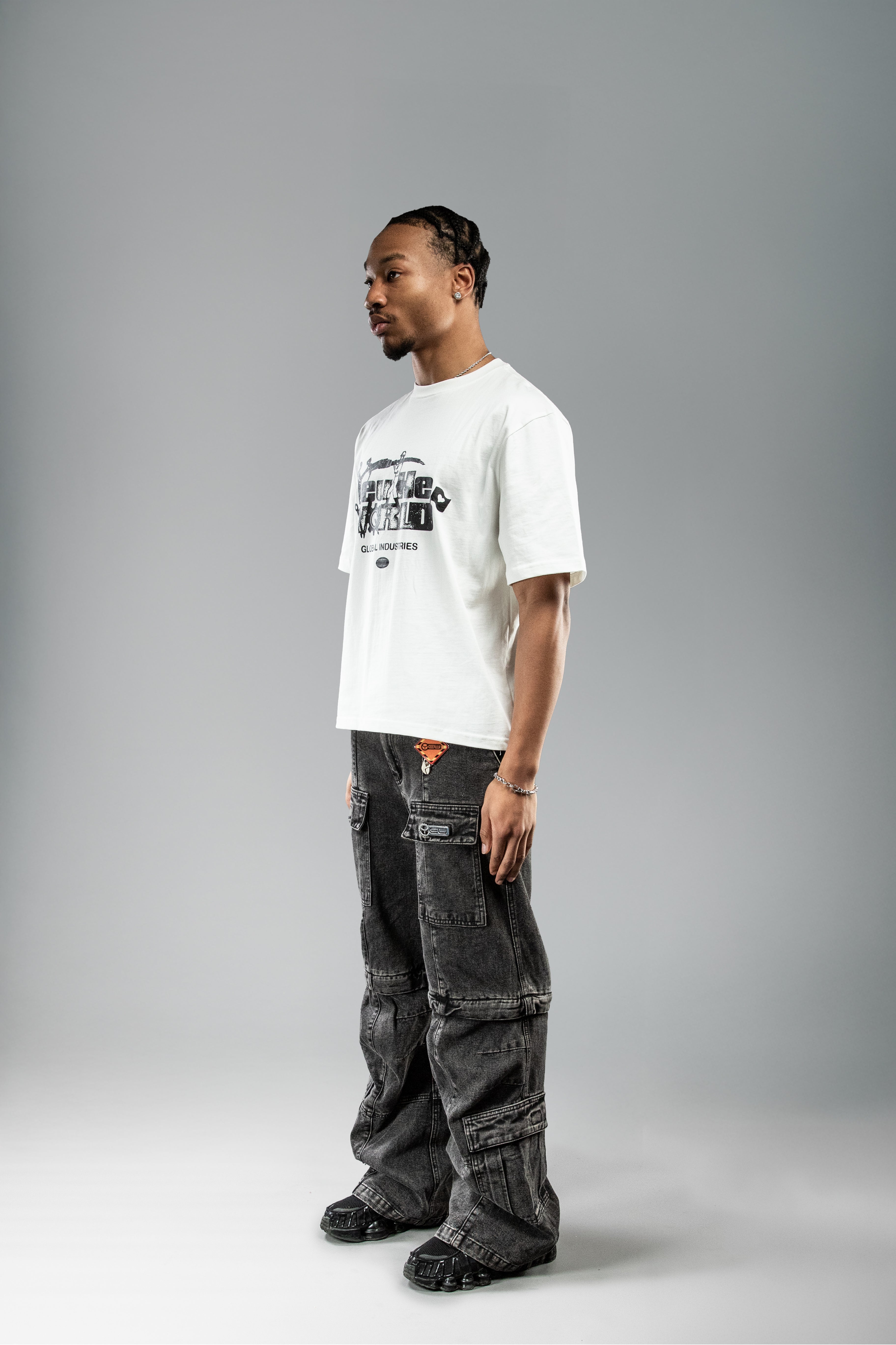 Weißes T-Shirt mit schwarz illustriertem Frontprint, getragen in seitlicher Pose. Der Print ist gut sichtbar, die Kombination erfolgt mit weiter, gewaschener Cargo-Hose.
