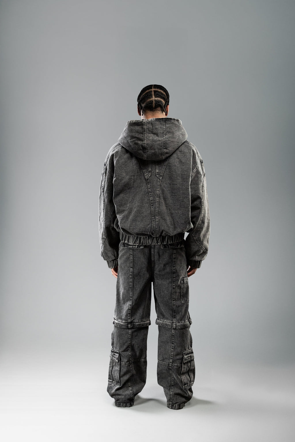 Die Hose zeigt auf der Rückseite eine dezente Taschenstruktur und Teilungsnähte auf der unteren Beinpartie. Der lockere Schnitt reicht bis über die Schuhe, wodurch die weite Silhouette betont wird.