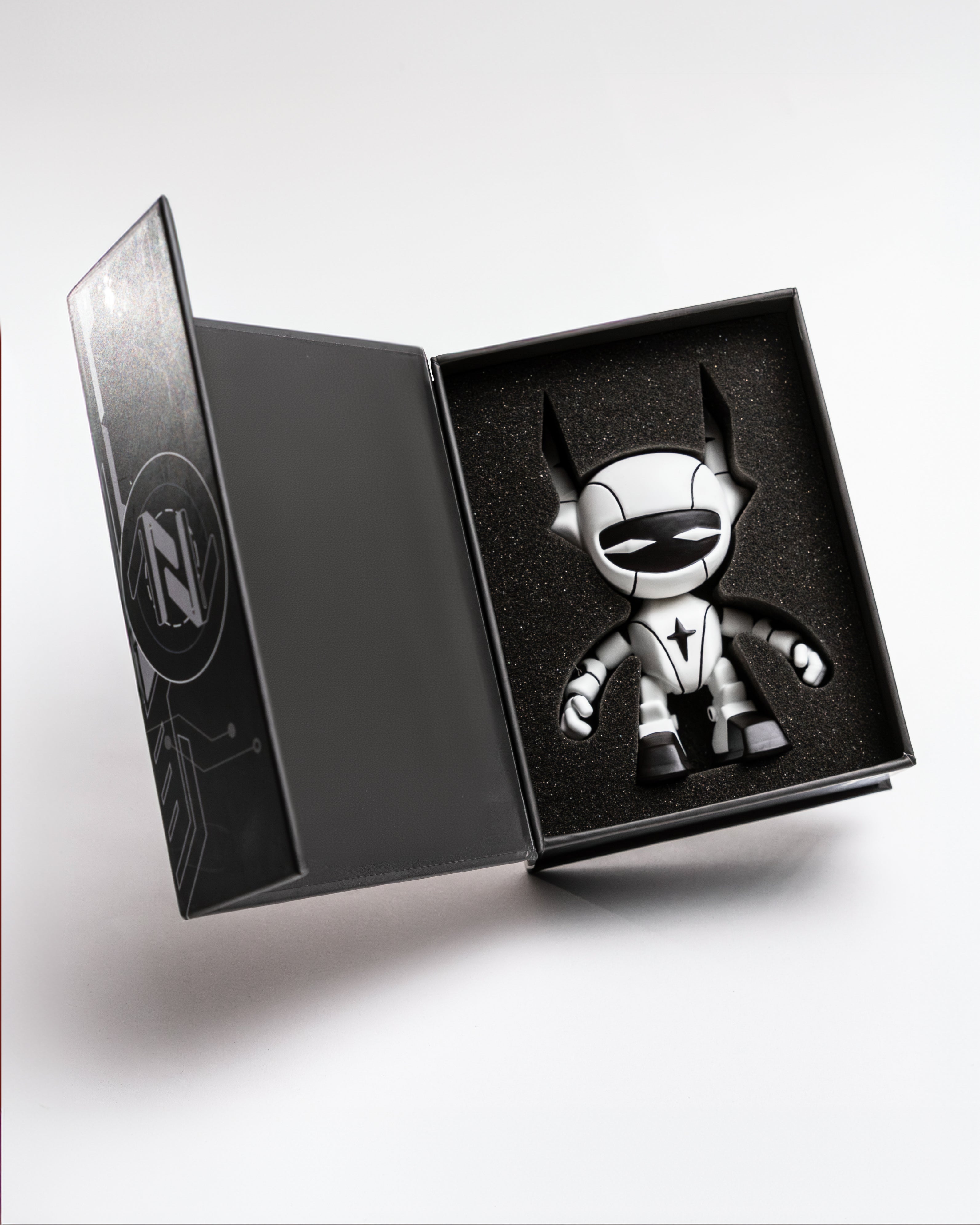 Die Verkaufsverpackung der Figur in Schwarz mit technischen Schaltkreislinien. Links ist ein stilisiertes YEU-Logo zu sehen, rechts eine grafische Darstellung des Roboterkopfes. Die Aufschrift lautet: „YEU.THEWORLD“ und „YEU.THE WORLD FOUNDERS EDITION ROBOT“.